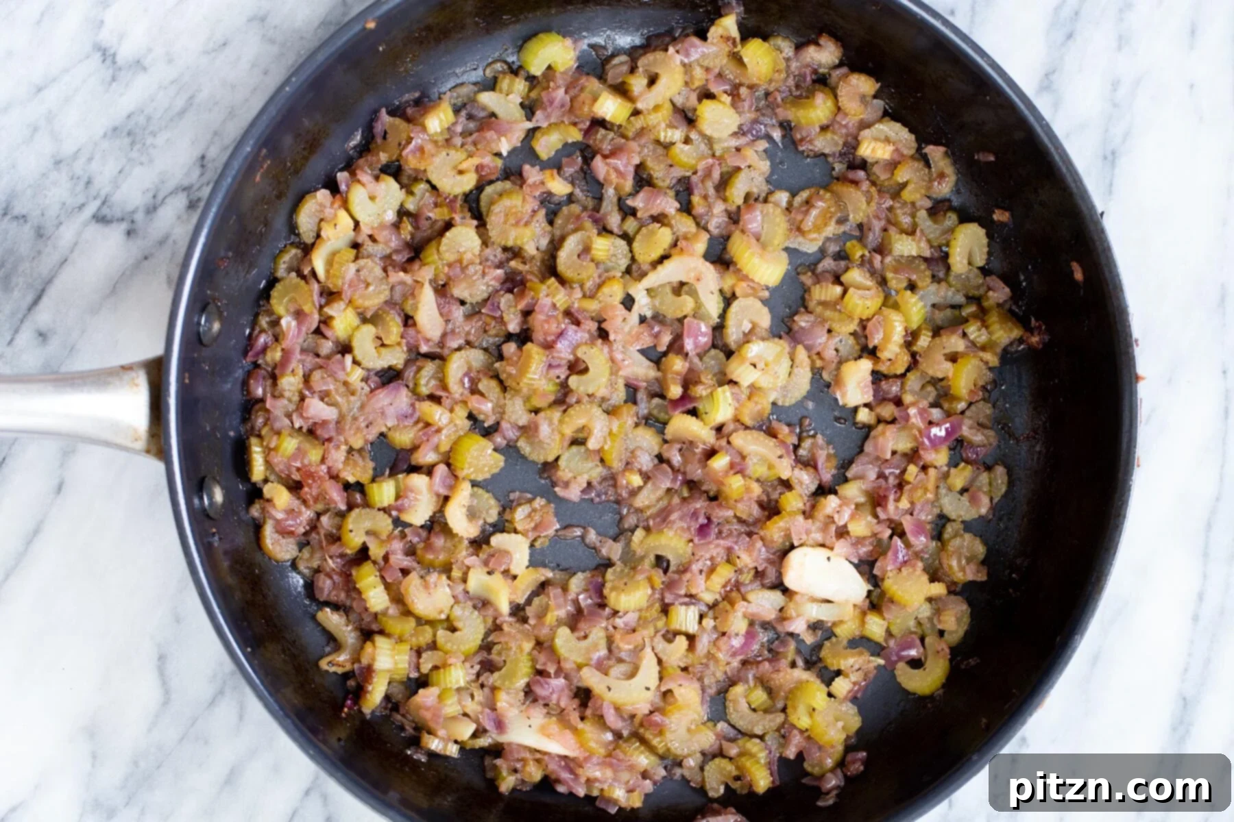Chopped onions and celery sautéing in a black pan, forming the aromatic base for the vegan stuffing.
