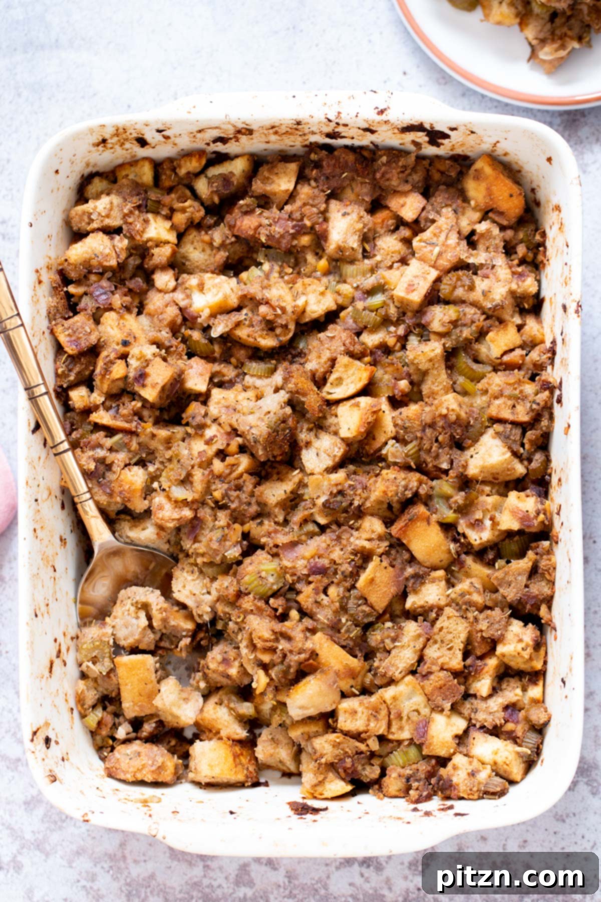 A top-down view of vegan stuffing with chickpea sausage in a white casserole dish, garnished with fresh herbs.