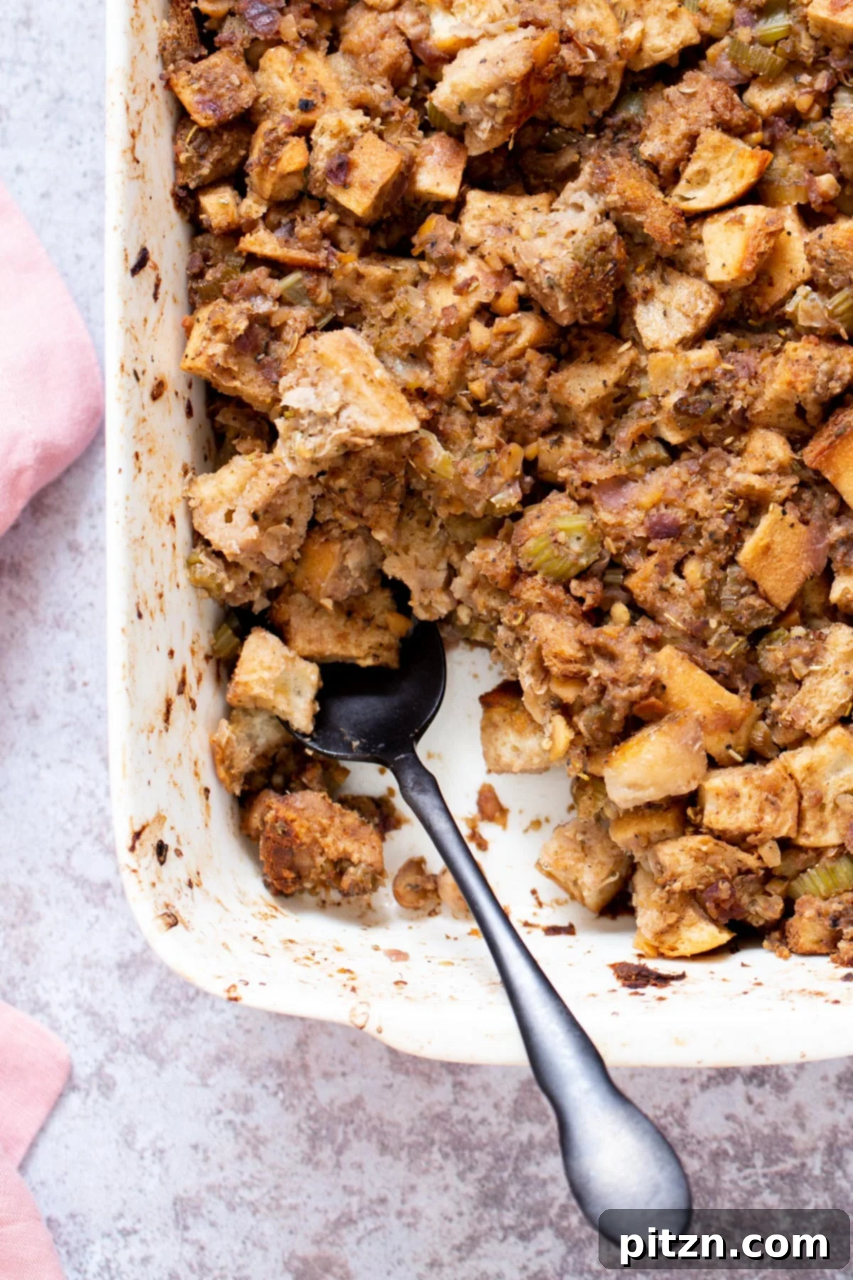 A serving spoon lifting a portion of hot vegan stuffing from a white casserole dish, showcasing its texture.