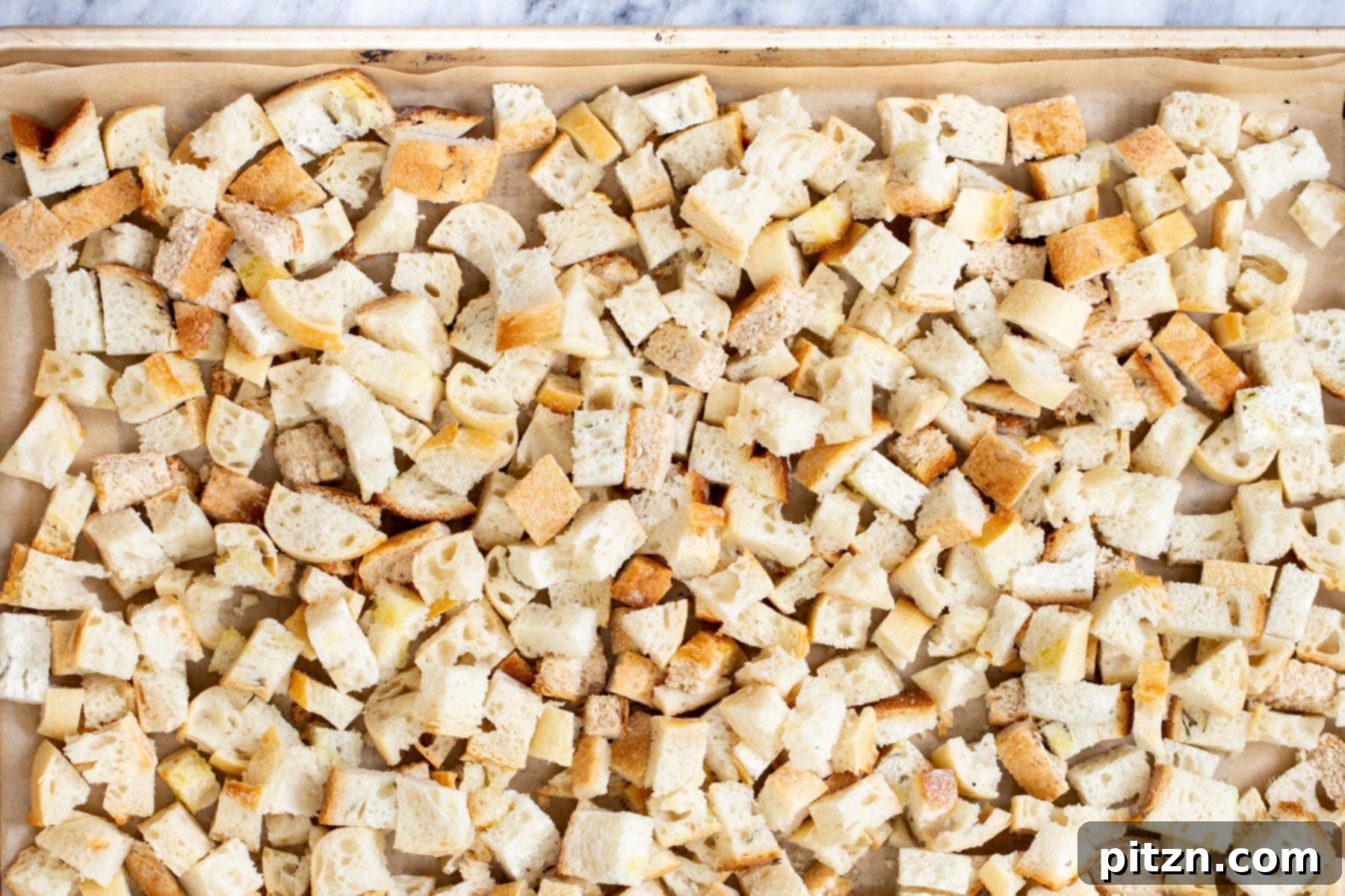 Evenly cut vegan bread cubes arranged on a parchment-lined baking sheet, ready for toasting.