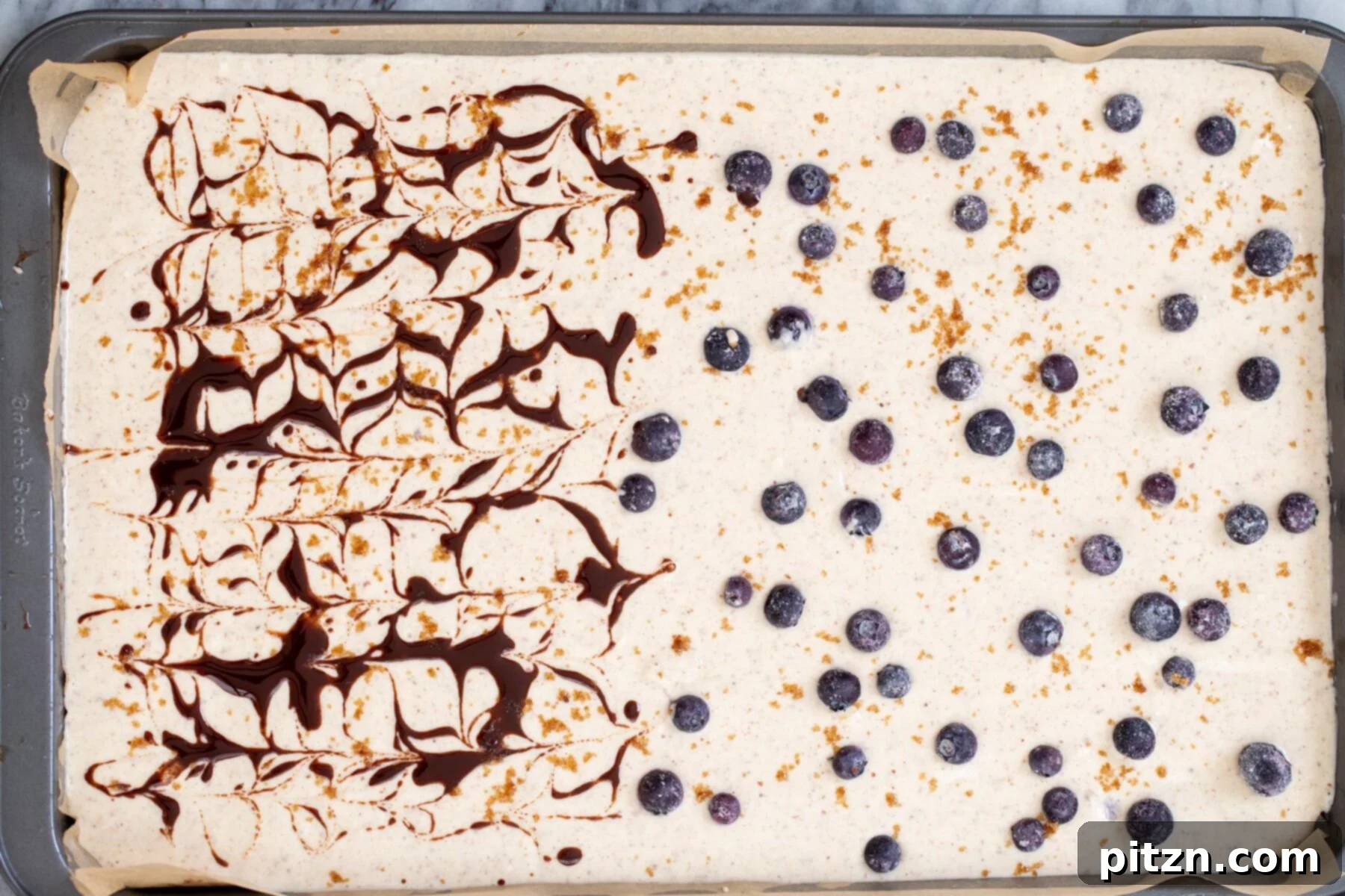 vegan sheet pan pancakes a sheet pan with pancake batter half topped with blueberries, half swirled with cinnamon syrup