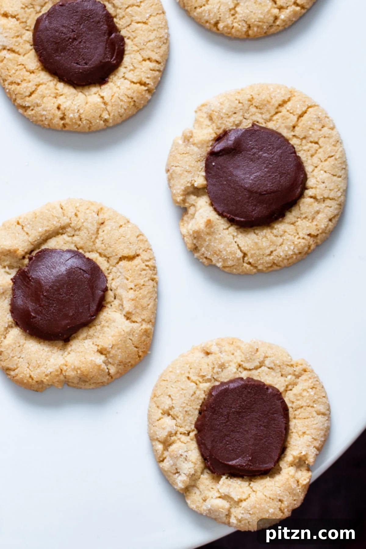 Delicious Chocolate-Filled Gluten-Free Thumbprint Cookies Finished vegan gluten-free thumbprint cookies with melted chocolate centers on a white plate.