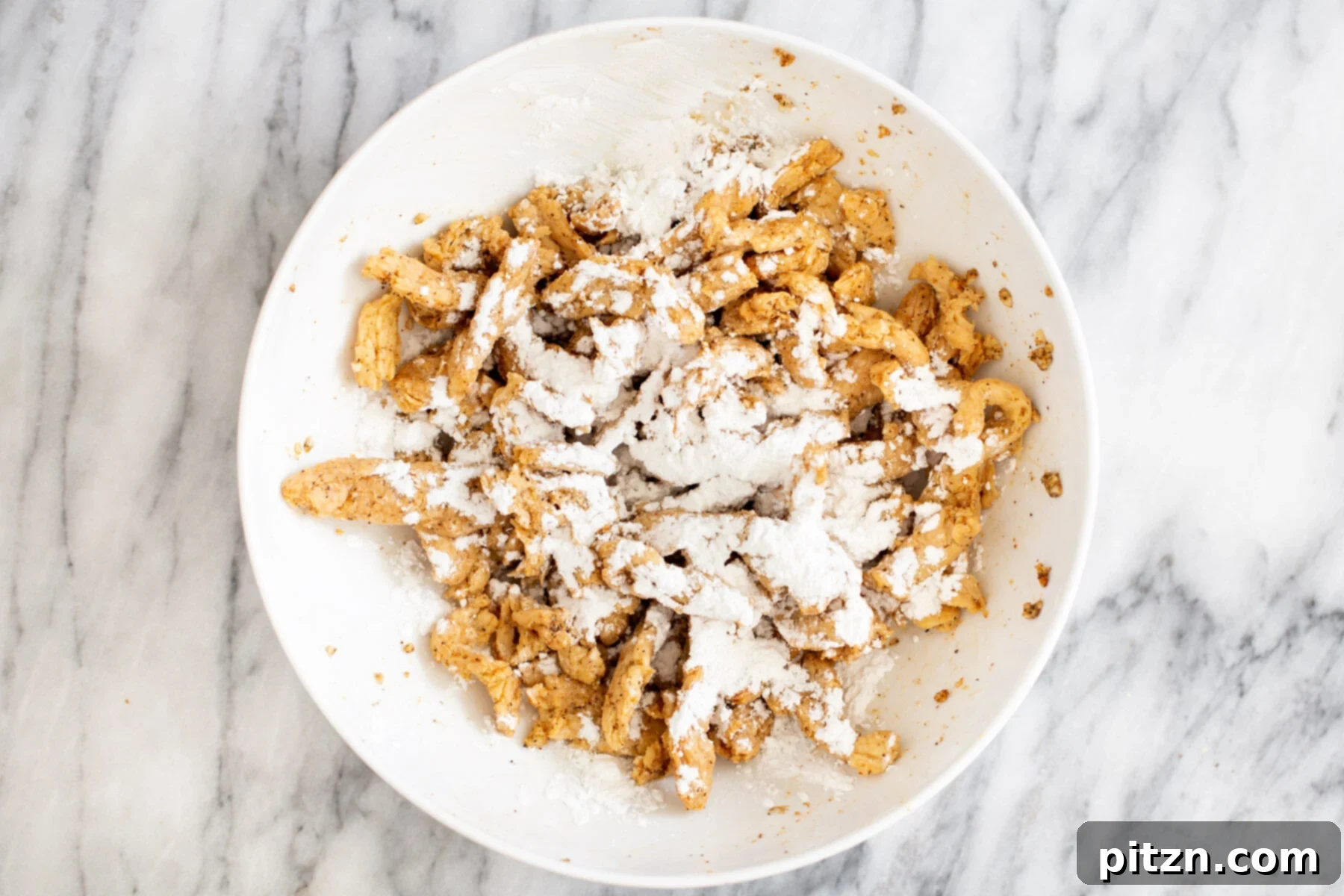 Marinated soycurls lightly dusted with cornstarch in a bowl, preparing them for baking or pan-frying.