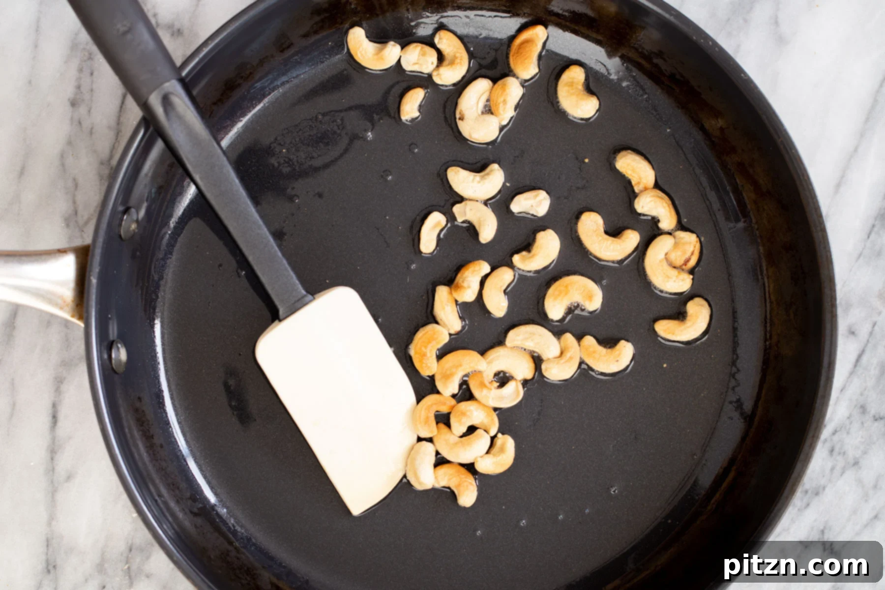 Raw cashew nuts browning in a teaspoon of oil in a black sautéing pan, a key step for the sauce.