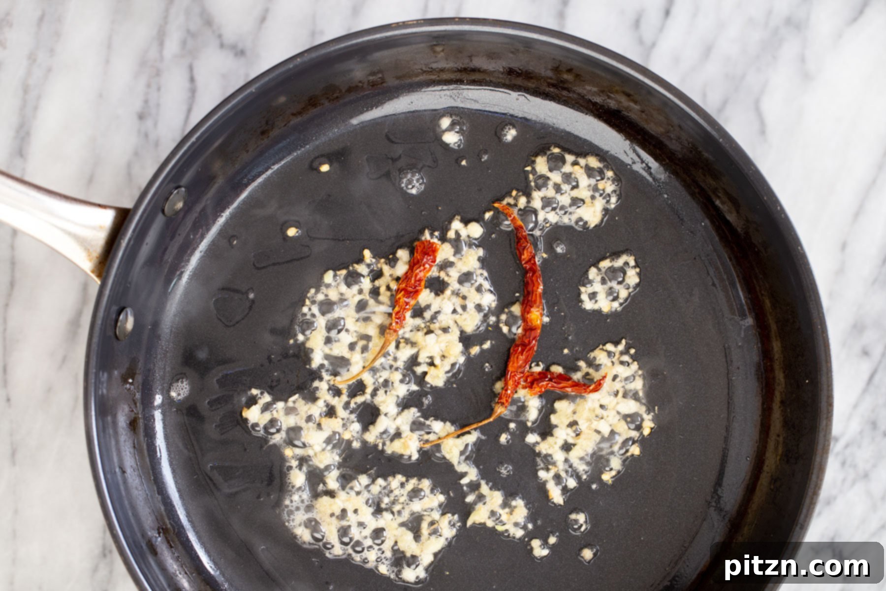 Sautéed garlic, ginger, and chilies in a frying pan, ready for the next layer of vegetables.