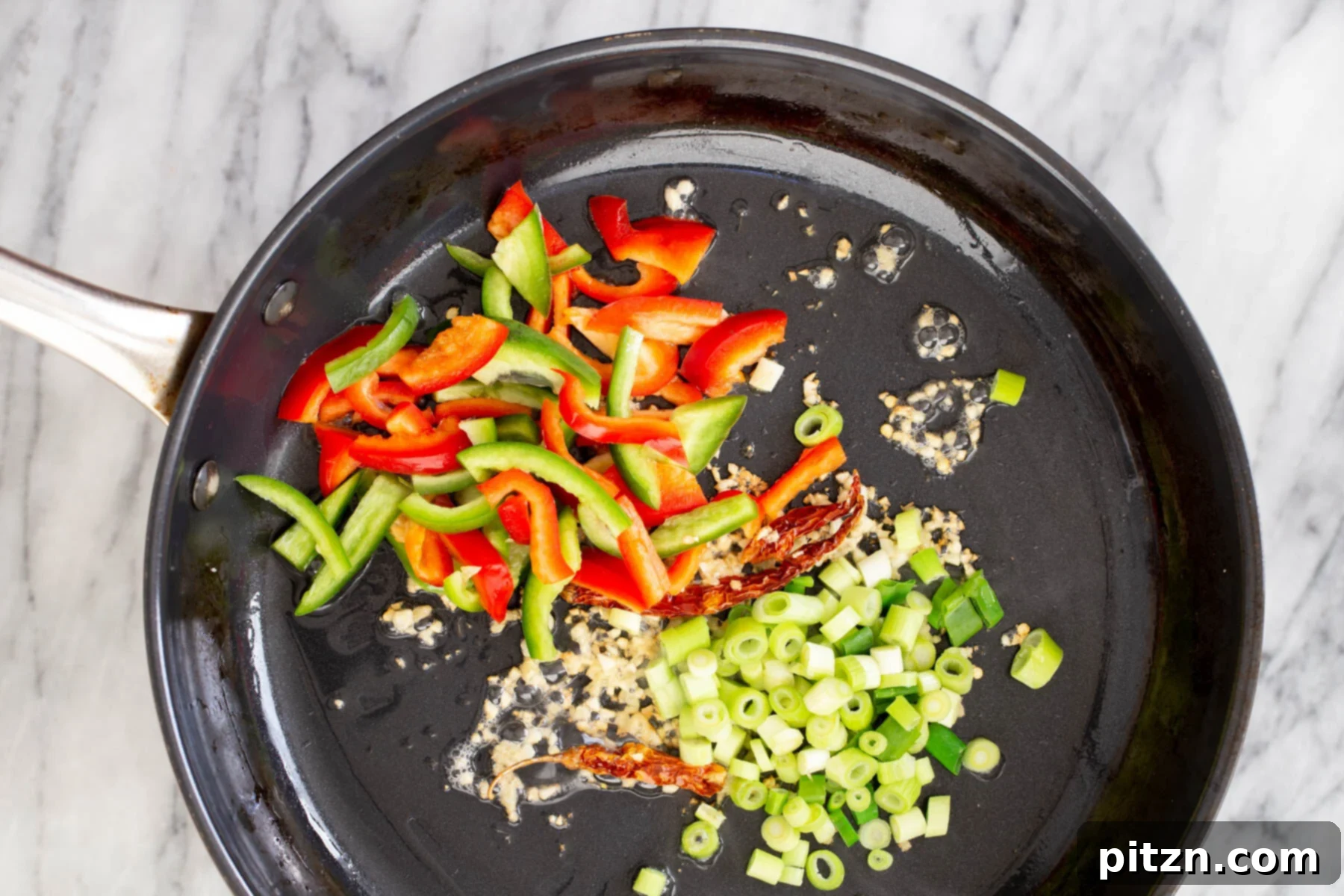 Vibrant bell peppers, white parts of green onions, and garlic stir-frying in a pan, releasing their aromas.