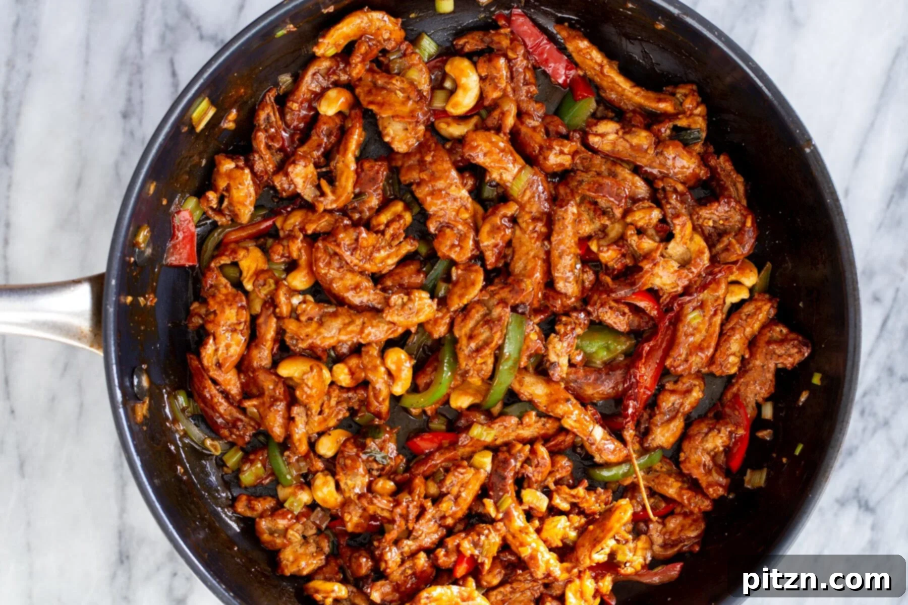 Soycurls, cashews, and bell peppers fully mixed with the sweet and spicy sauce in a frying pan, indicating the dish is complete.