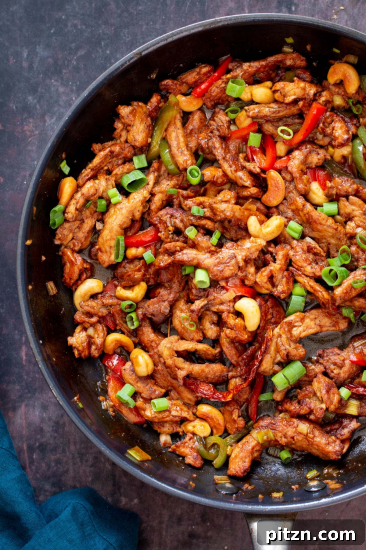 Vegan soycurls coated in a glossy, sweet, and spicy gravy, adorned with toasted cashew nuts and vibrant bell peppers, presented beautifully.