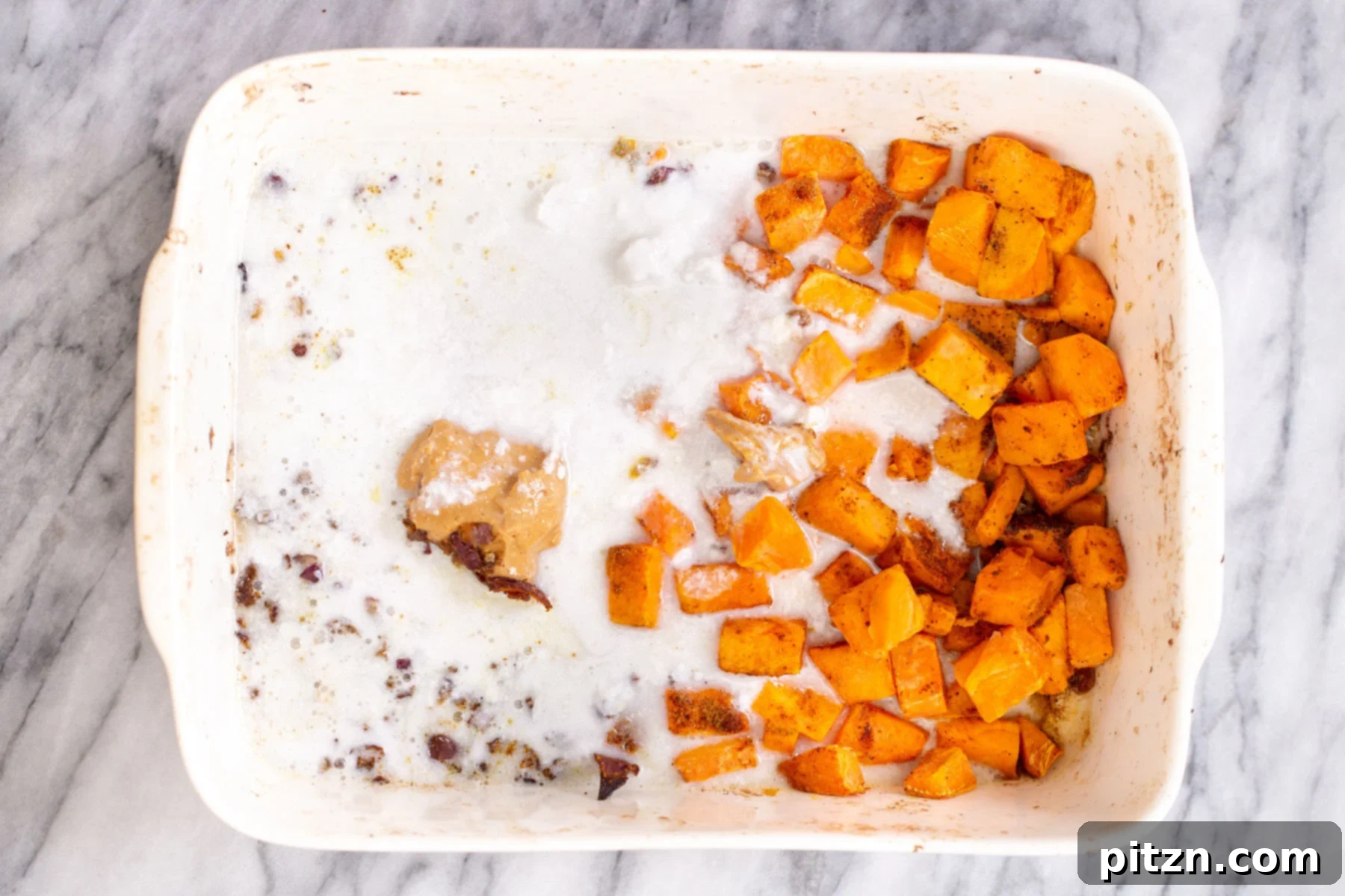 Sweet Potato and Chickpea Curry Bake 9 Thick coconut milk and creamy peanut butter being poured and dolloped into a casserole dish with partially baked sweet potatoes and onions, ready to be stirred
