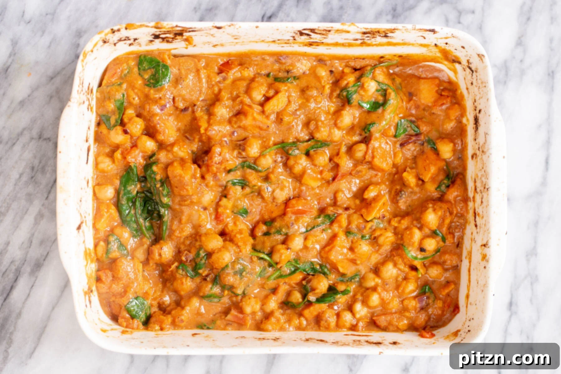 chickpea sweet potato curry Fresh baby spinach being gently stirred into the steaming hot, creamy sweet potato chickpea curry directly in the casserole dish, wilting from the heat