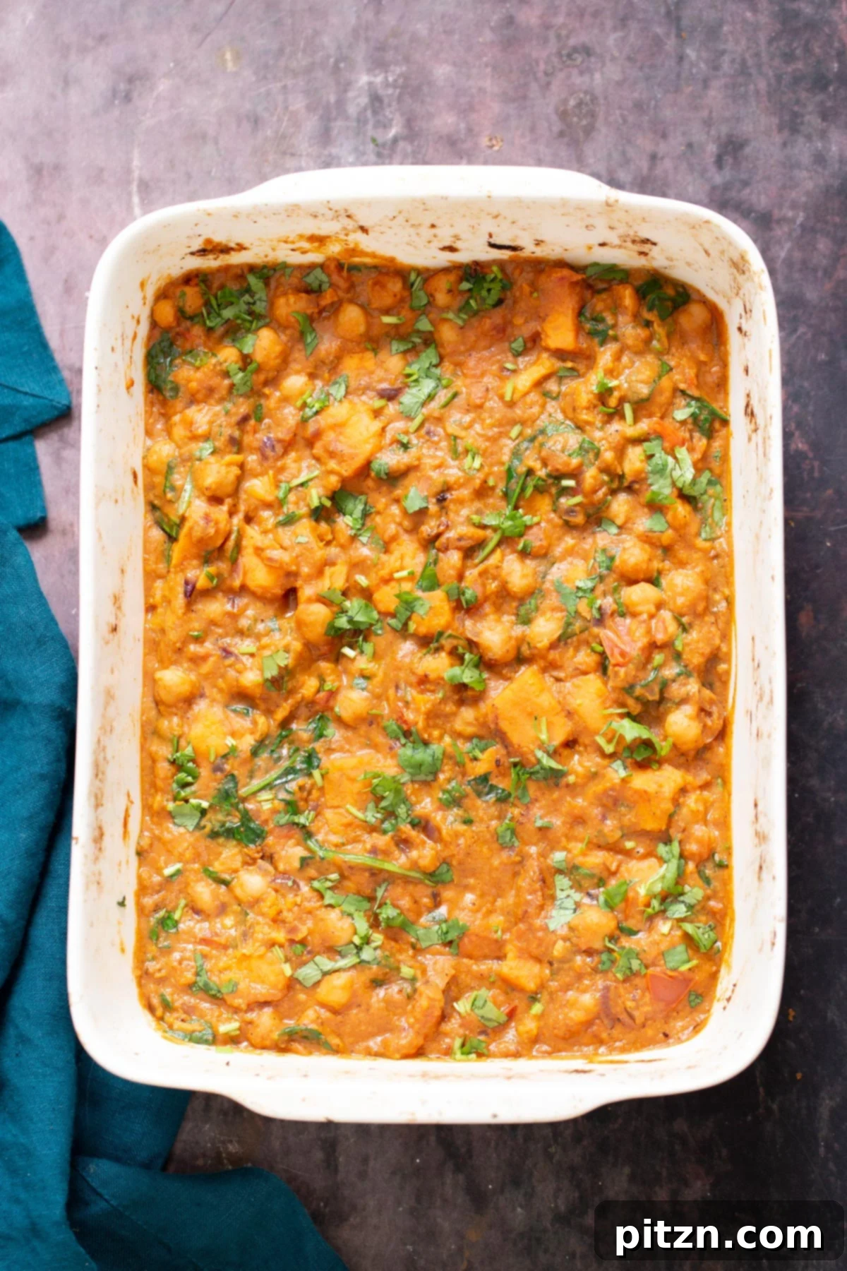 Sweet Potato and Chickpea Curry Bake 3 Top-down view of a rectangular casserole dish filled with baked chickpea sweet potato curry, a blue-green kitchen napkin resting beside it