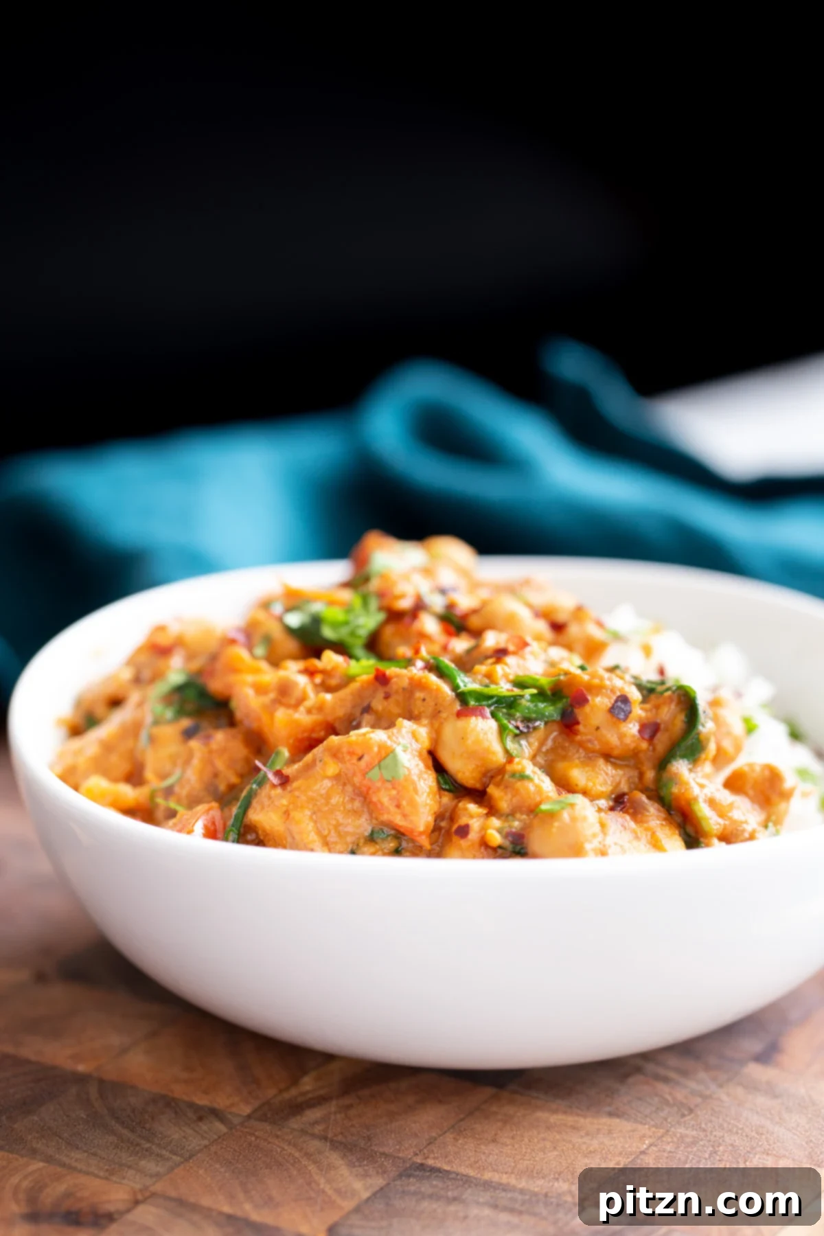 sweet potato chickpea curry Side view of a serving bowl filled with vibrant vegan chickpea sweet potato curry, accompanied by a bed of white rice