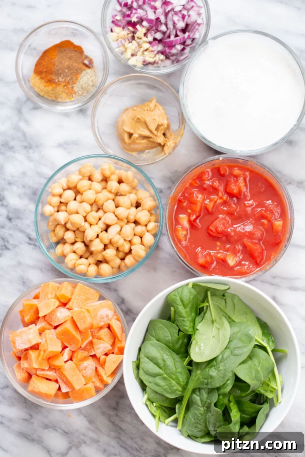 Sweet Potato and Chickpea Curry Bake 6 Various fresh ingredients including sweet potatoes, onions, garlic, ginger, and spices, laid out on a kitchen counter, ready for preparing vegan chickpea sweet potato curry