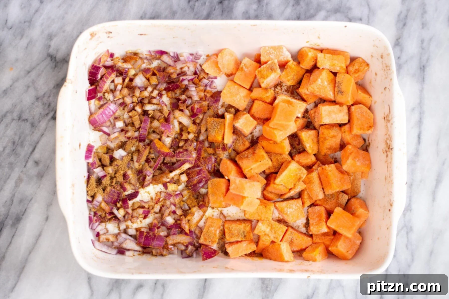 Sweet Potato and Chickpea Curry Bake 7 A casserole dish prepared with diced sweet potato cubes on one side, and a mix of chopped onions, minced garlic, and ginger on the other side, before baking