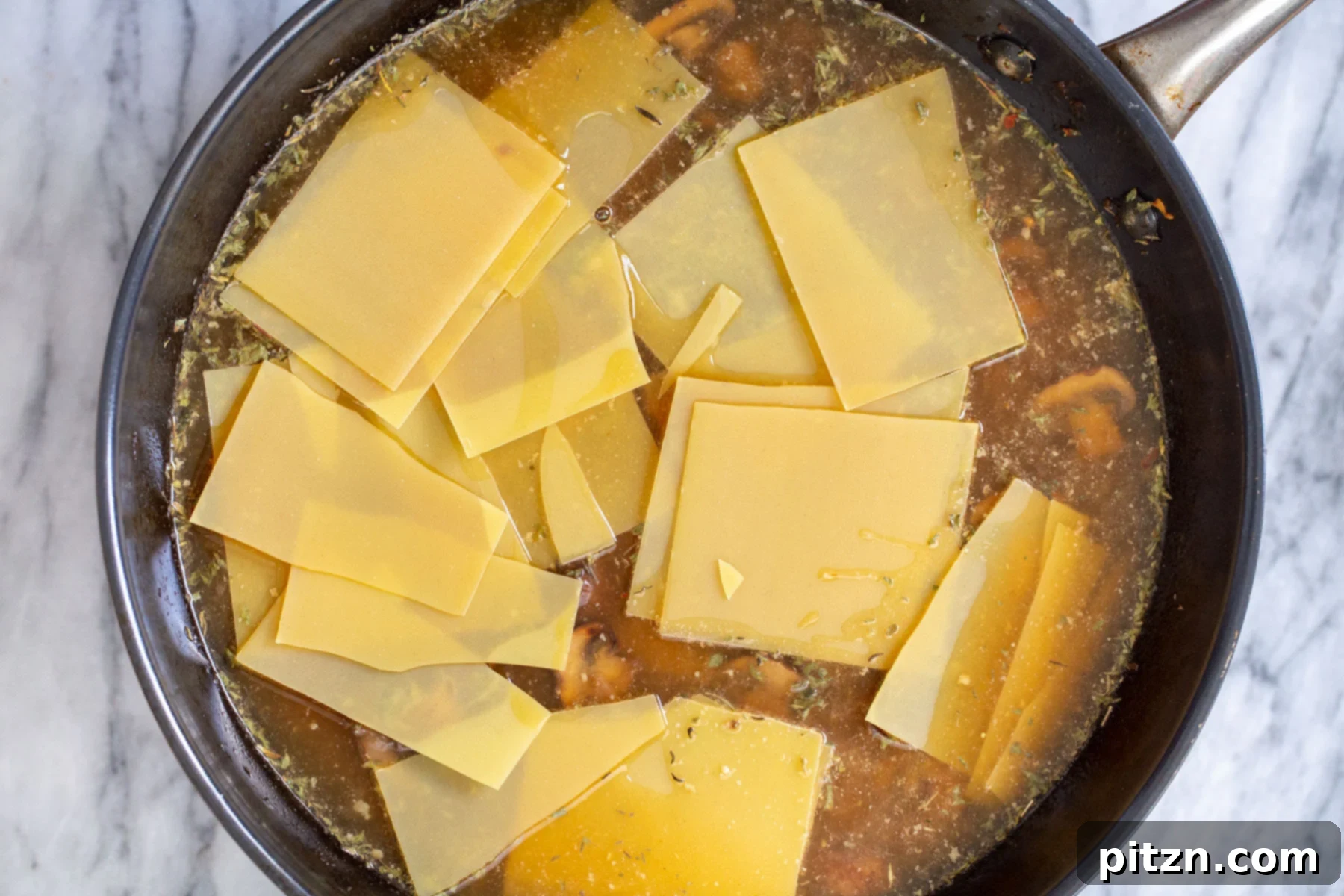 Effortless One-Pan Vegan White Lasagna with Tofu Bechamel 14 broken lasagna noodles being added to a skillet with mushroom broth