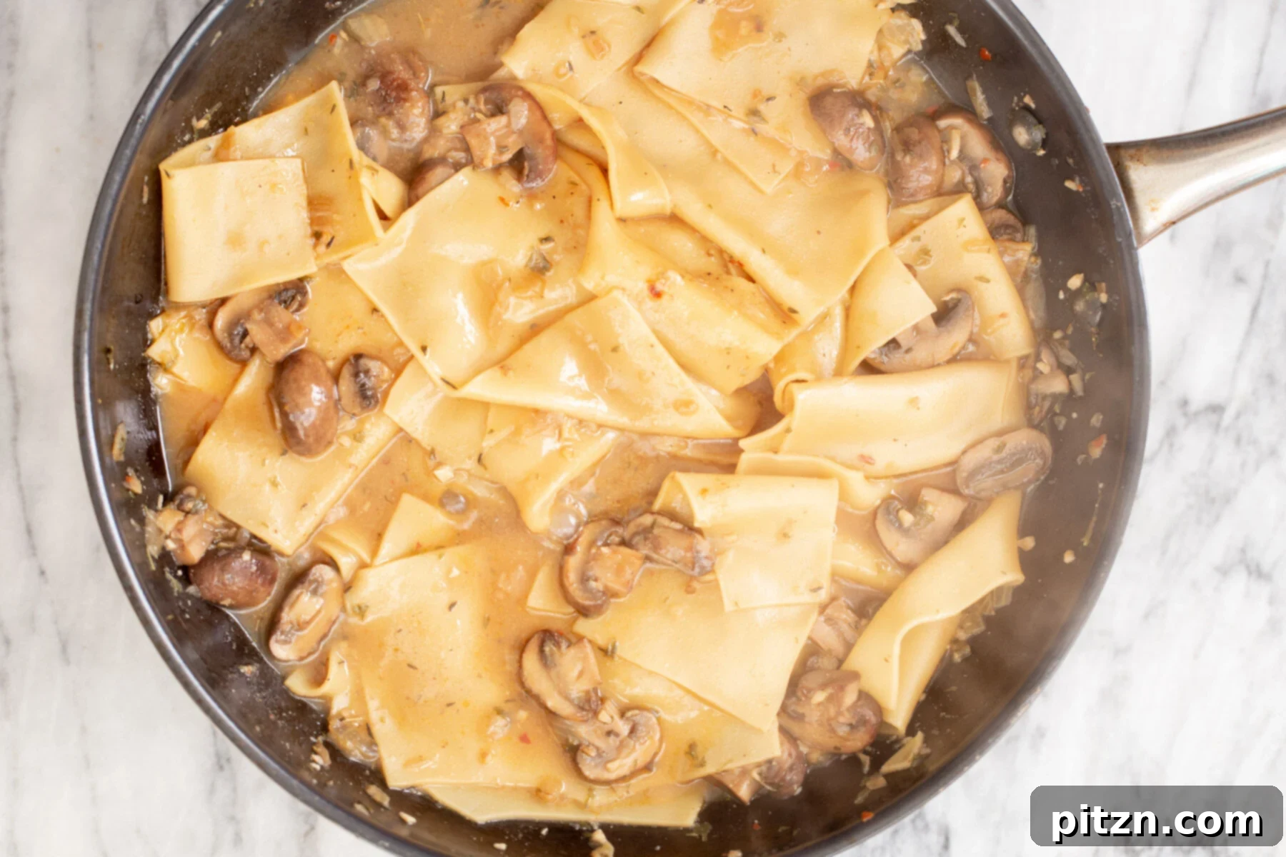 Effortless One-Pan Vegan White Lasagna with Tofu Bechamel 16 mushroom gravy and cooked broken lasagna noodles in a skillet