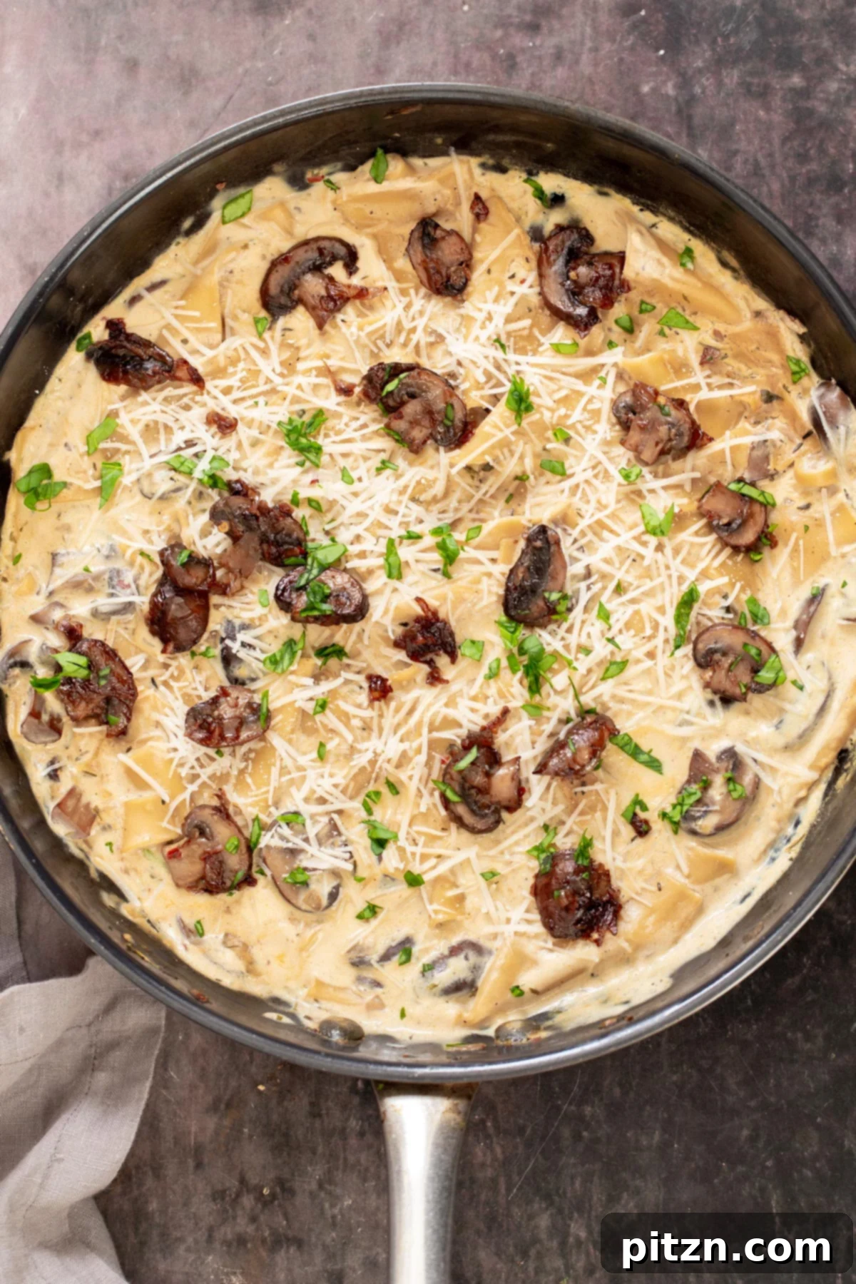 Effortless One-Pan Vegan White Lasagna with Tofu Bechamel 3 vegan parmesan cheese being sprinkled on top of a vegan white skillet lasagna with balsamic mushrooms