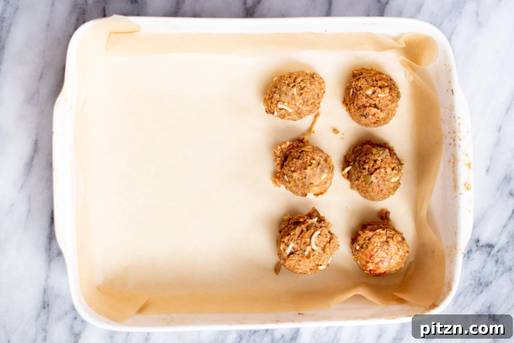 Rows of freshly rolled vegan lentil meatballs arranged neatly on a parchment-lined baking dish