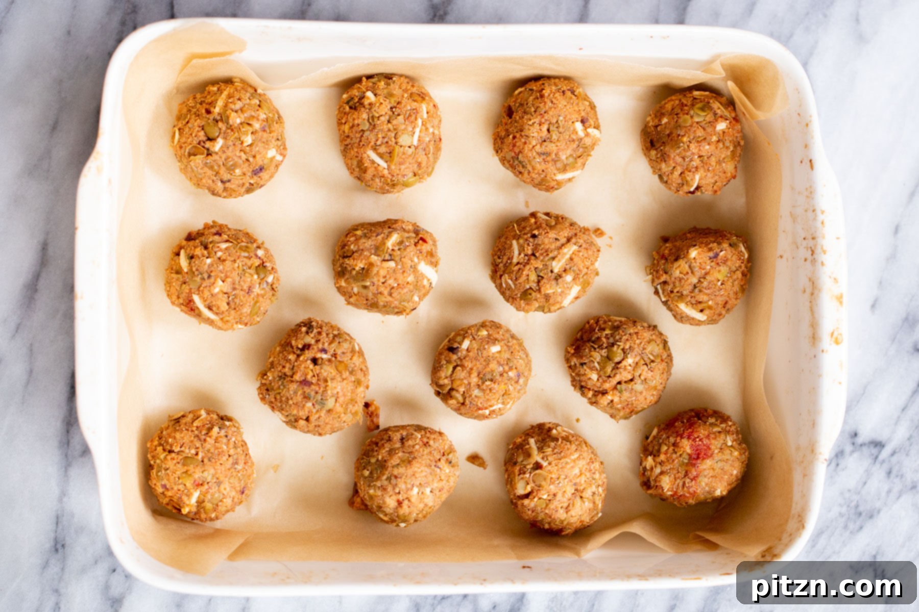 Vegan lentil meatballs in a baking dish, lightly sprinkled with vegan cheese before baking for extra flavor