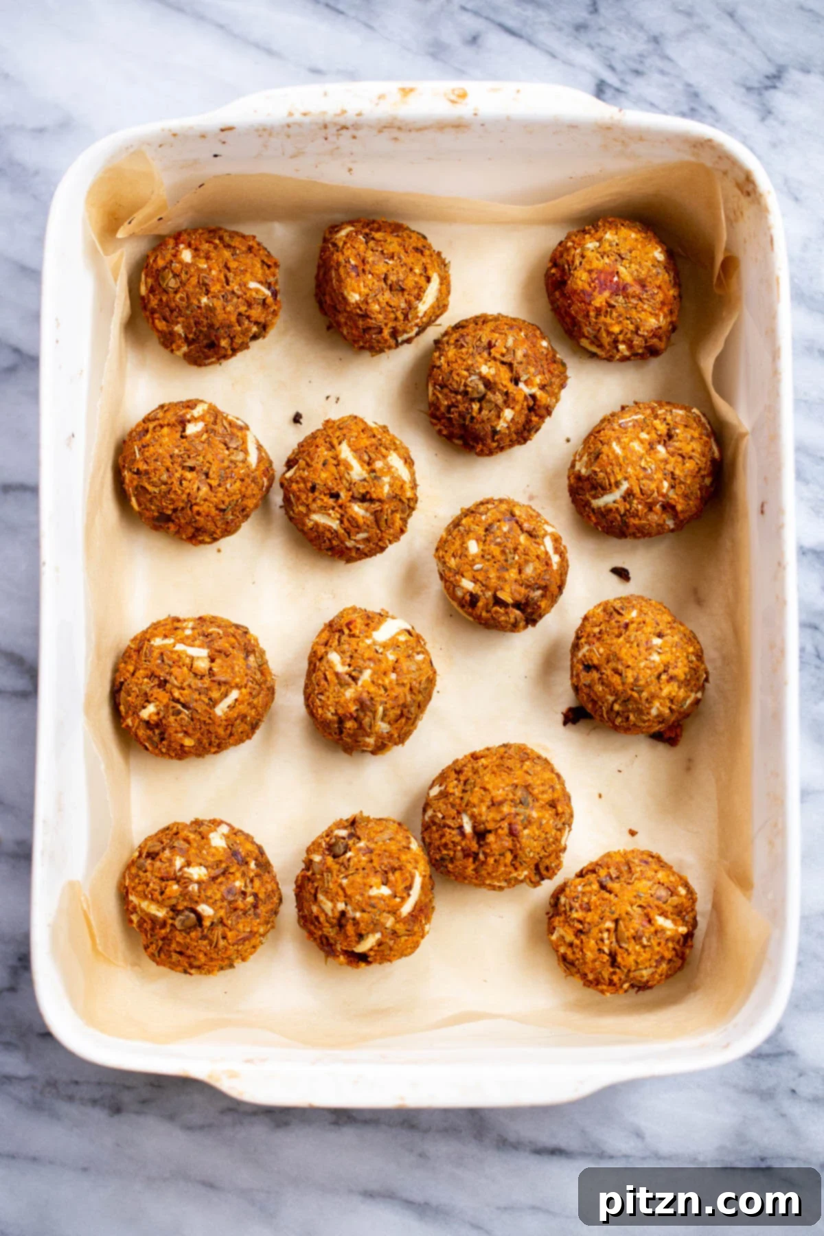 A baking dish filled with golden-brown, perfectly baked vegan lentil meatballs, ready for assembly into subs