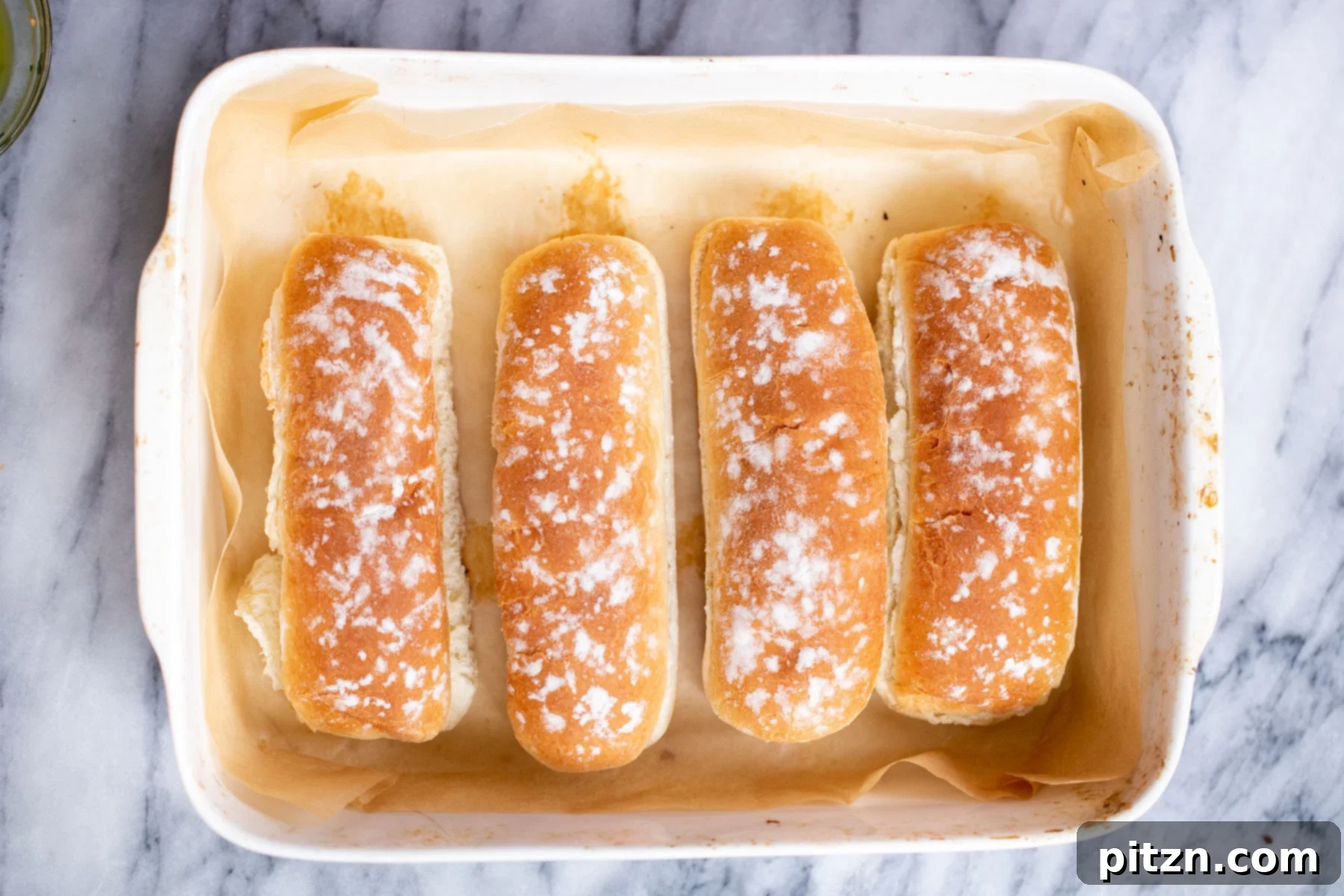 Four split long buns arranged in a baking dish, ready for toasting and filling with delicious vegan meatballs