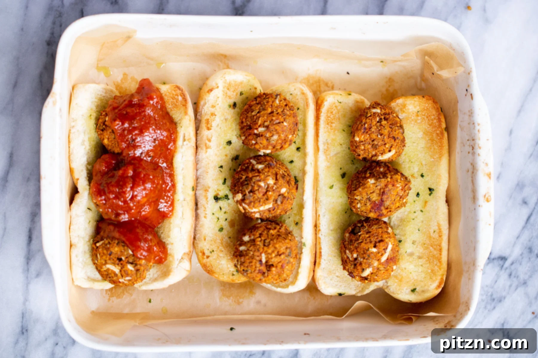 A casserole dish with vegan meatball subs being assembled, showing lentil meatballs covered in marinara sauce in toasted buns