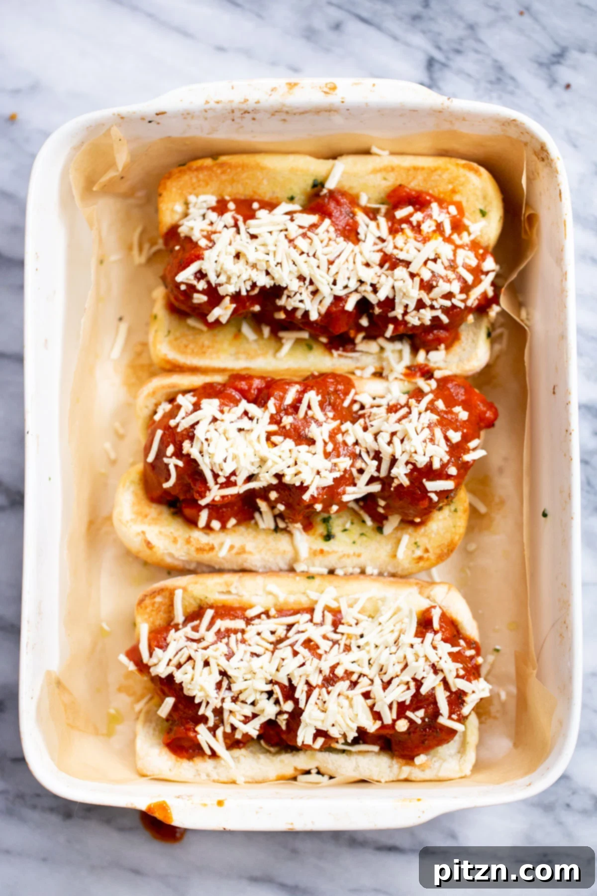 A baking dish showcasing finished vegan meatball subs, topped with perfectly melted vegan cheese and a sprinkle of fresh herbs