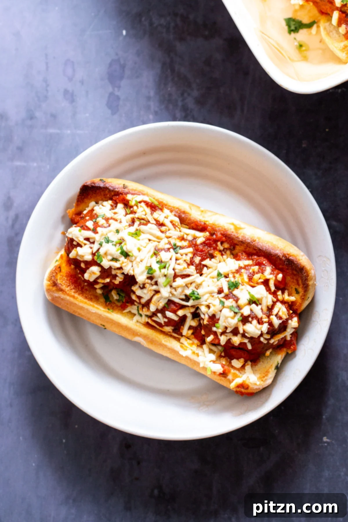 An overhead view of a single vegan meatball sub, garnished with fresh herbs and a generous sprinkle of vegan cheese shreds, showcasing its appetizing appeal