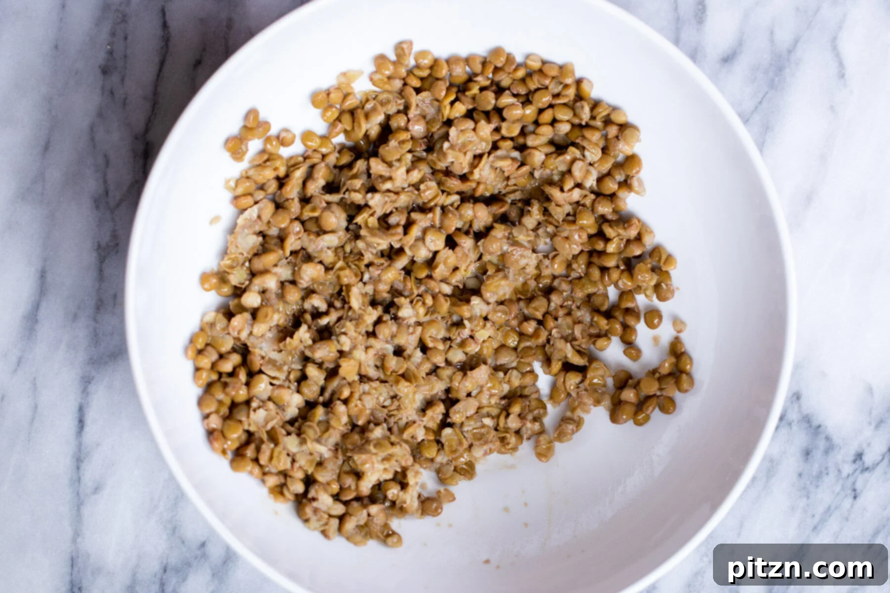 Cooked green lentils in a white mixing bowl, ready to be mashed for vegan meatballs