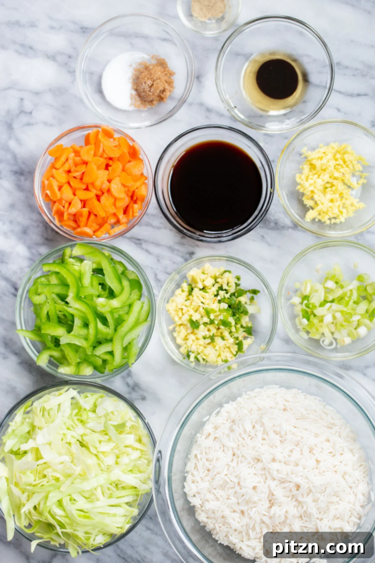 Indo Chinese Fried Rice A collection of fresh ingredients for Indo-Chinese Fried Rice, including carrots, bell peppers, ginger, garlic, chilies, and sauces, neatly arranged on a marble countertop.