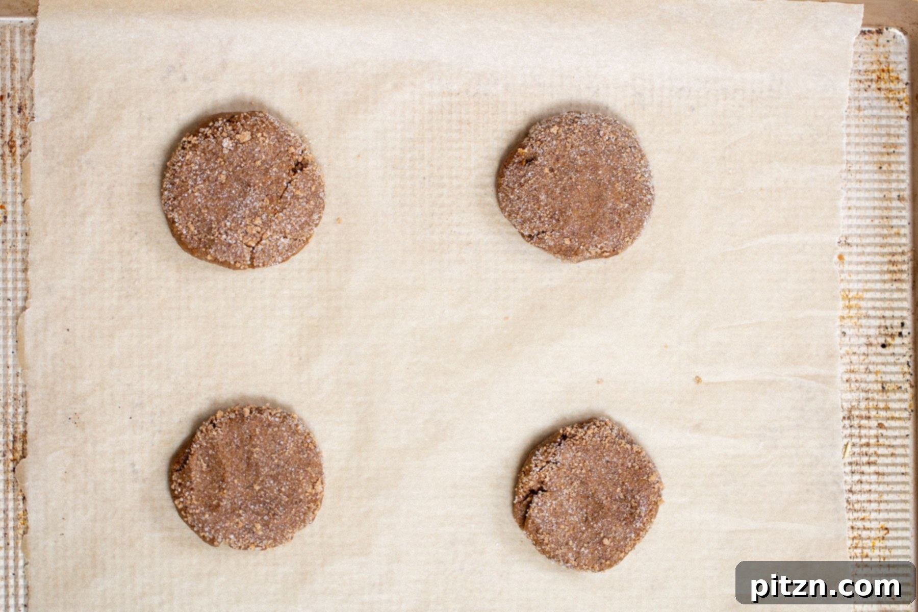 Unbaked vegan almond flour ginger molasses cookies, perfectly rolled and coated in sugar, arranged neatly on a parchment-lined baking sheet, ready for the oven. Grain-Free & Gluten-free.
