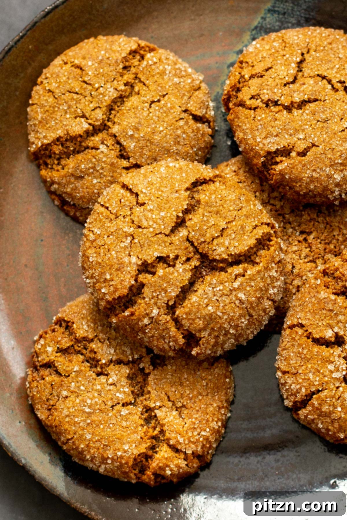 A close-up of almond flour ginger cookies with distinct crinkly tops, resting on a rustic brown plate, highlighting their perfectly baked texture and rich color.
