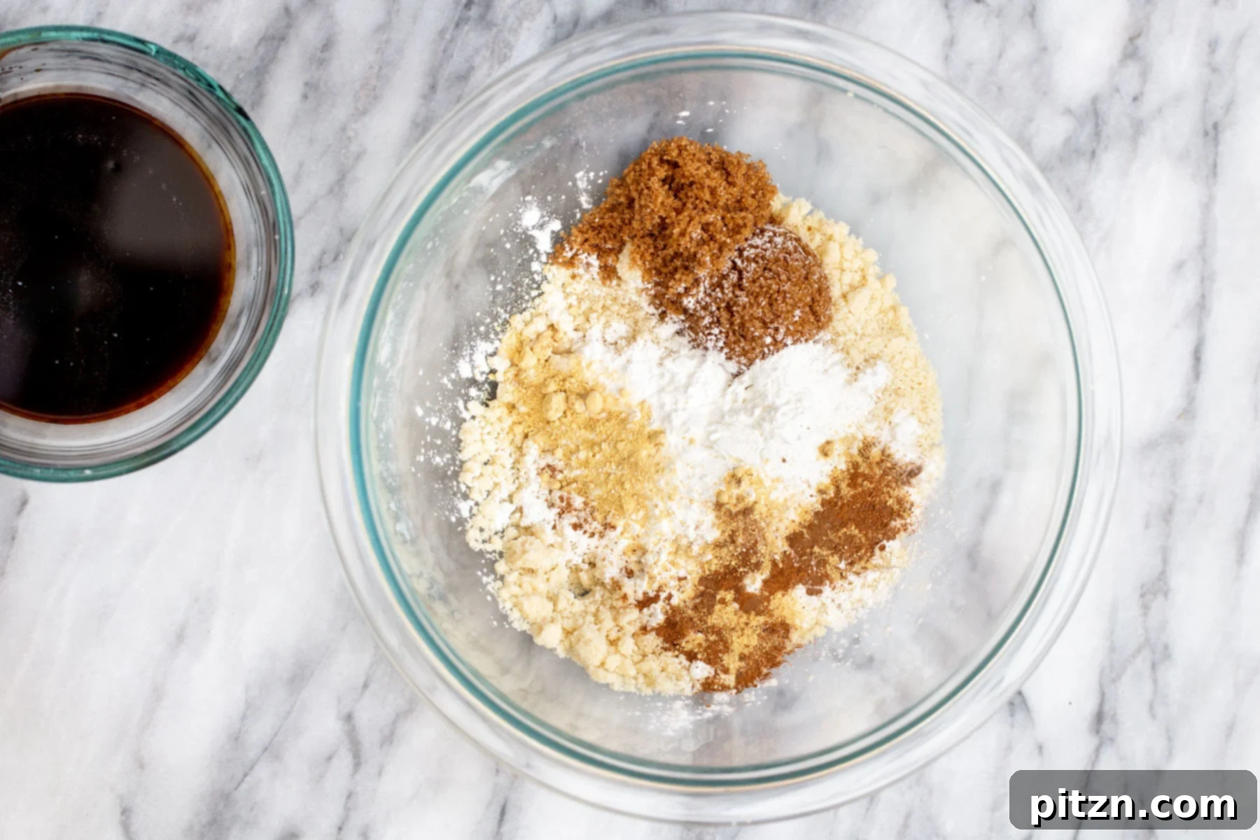 Dry ingredients perfectly mixed in a clear glass bowl, ready for the wet components of the vegan almond flour ginger molasses cookie dough.