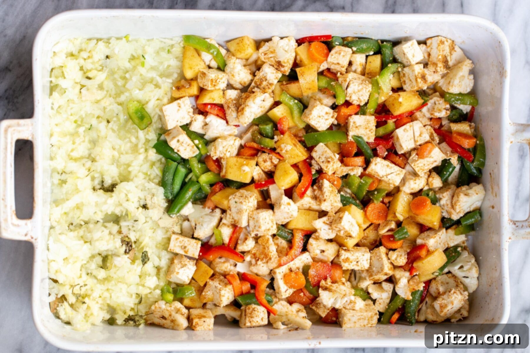 A white casserole dish filled with par-baked vegetables, tofu, and aromatics, with the onions starting to turn golden after the initial bake.