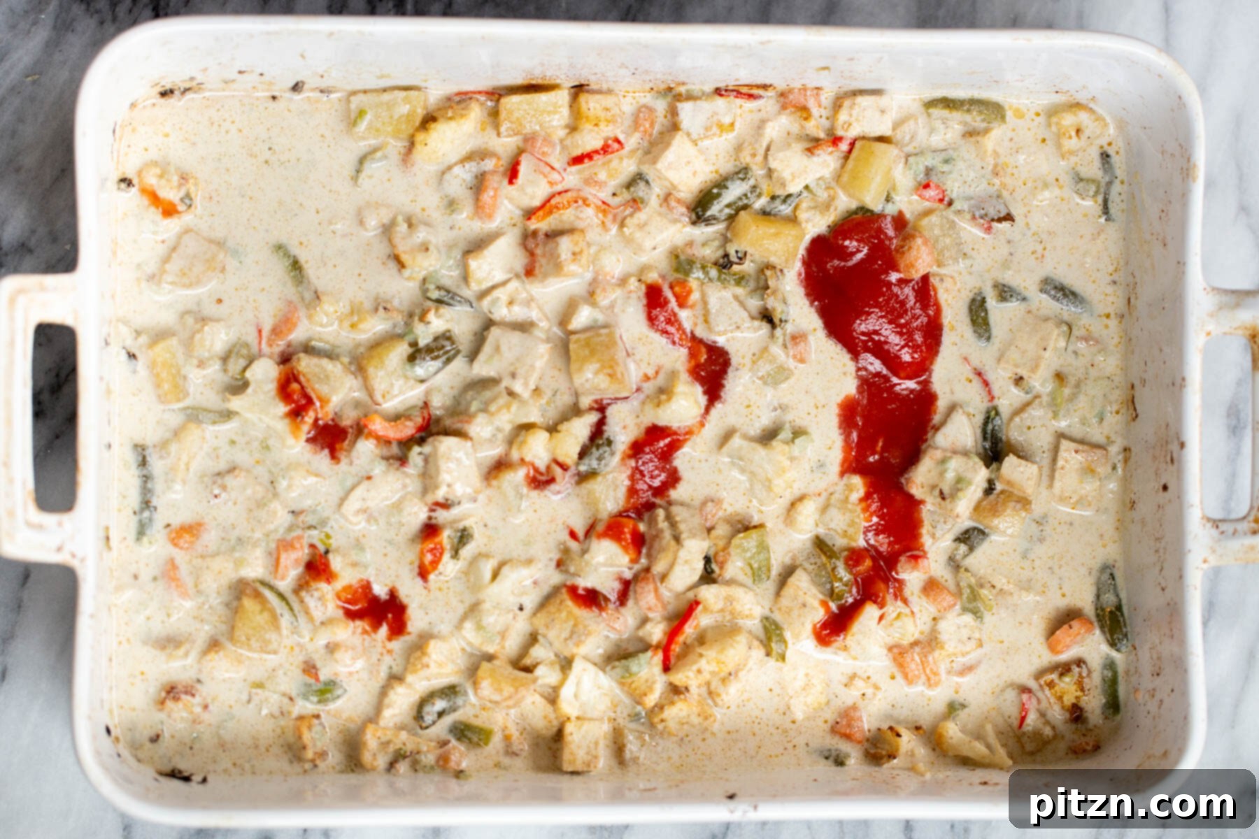 The baked Navratan Korma curry in a white casserole dish, with vegetables and tofu simmering in the creamy sauce, almost ready to serve.