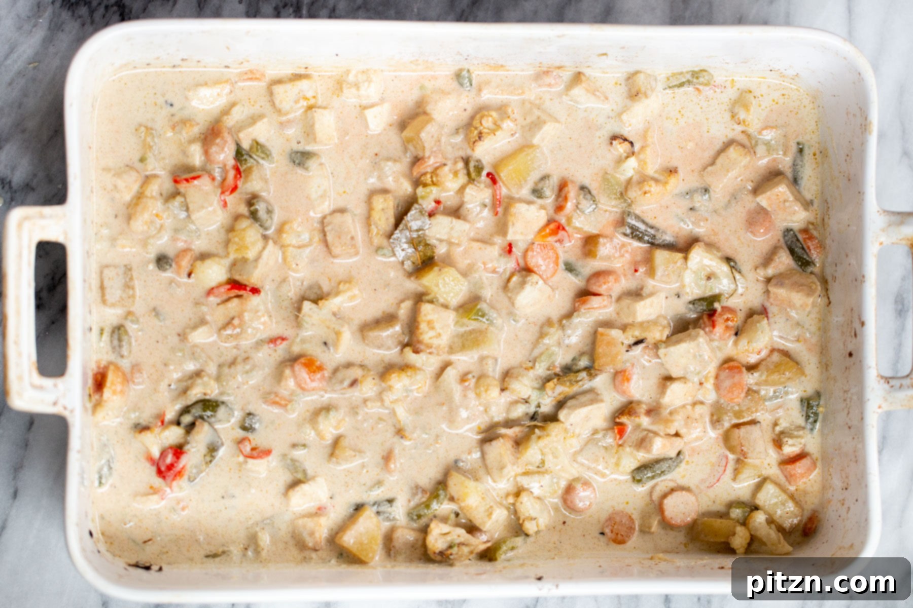 A beautifully baked Navratan Korma in a white casserole dish, rich with creamy sauce and colorful vegetables, ready to be served.
