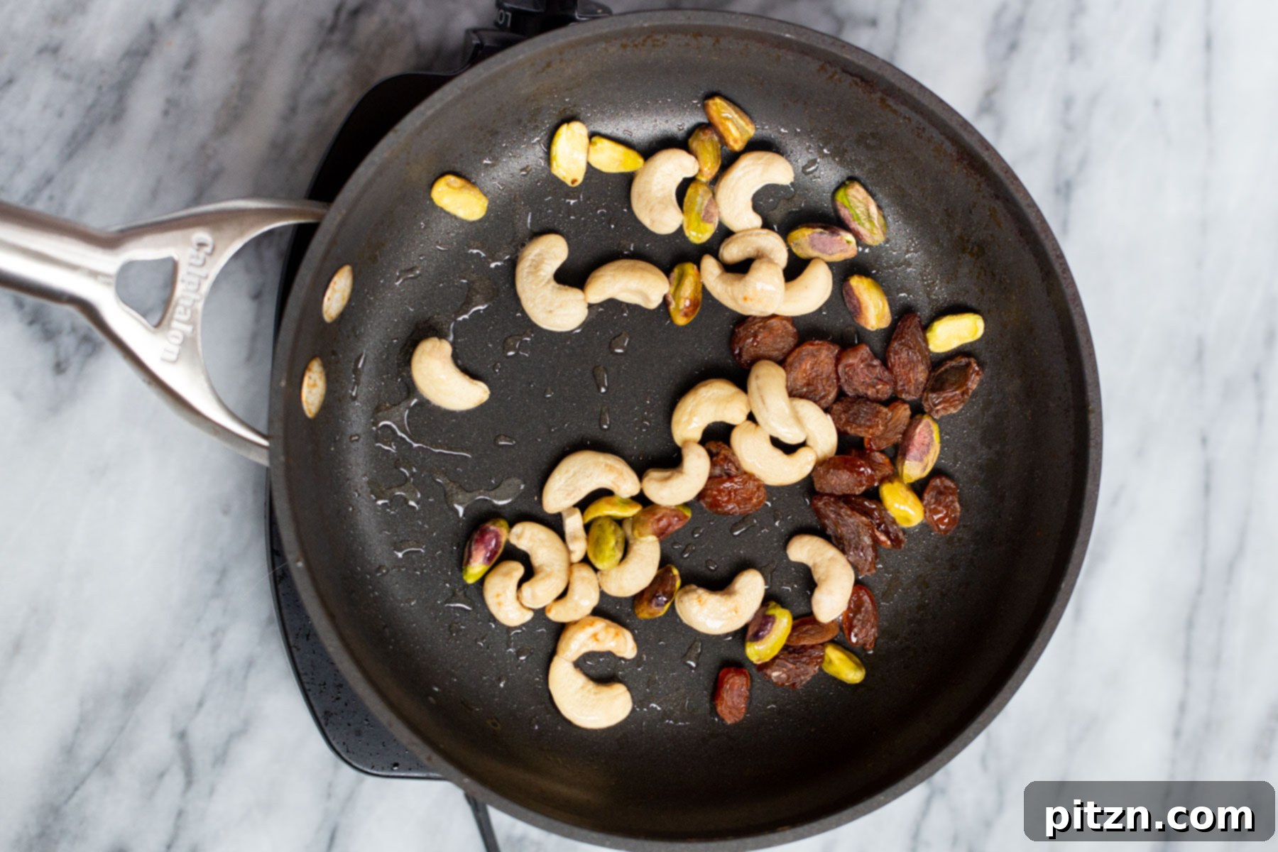 A black skillet filled with toasted nuts, golden brown and fragrant, prepared for garnishing the Navratan Korma.