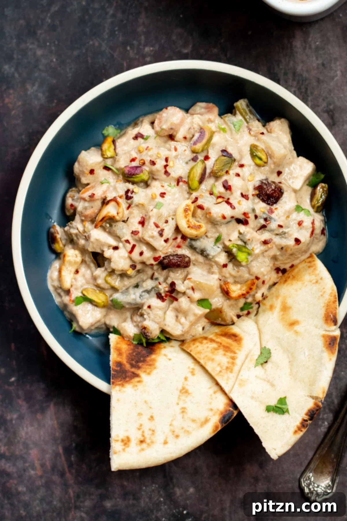 A beautifully presented bowl of Baked Vegan Navratan Korma, richly topped with chopped nuts and red chili flakes, showcasing its enticing texture.