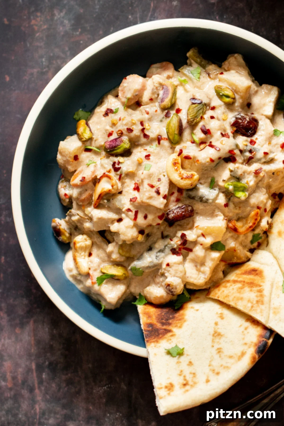 A bowl of creamy Indian Navratan Korma, generously sprinkled with vibrant red chili flakes, showcasing its rich texture.