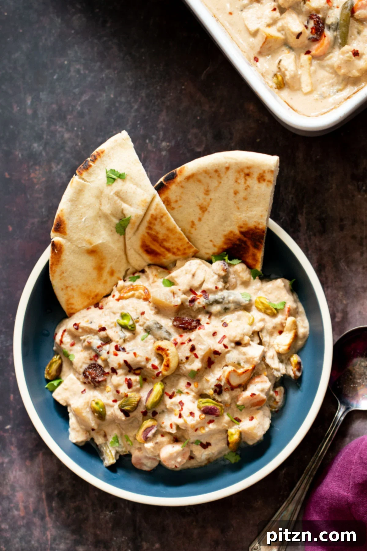 Vegan Navratan Korma elegantly presented in a white bowl, garnished with chopped nuts and fresh herbs, served alongside golden pita bread.