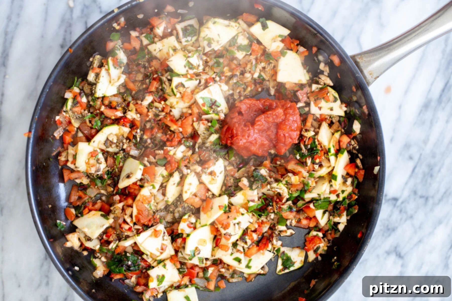 Tomato paste being added to a sautéing pan with a colorful mix of vegetables, deepening the flavor of the pasta sauce.