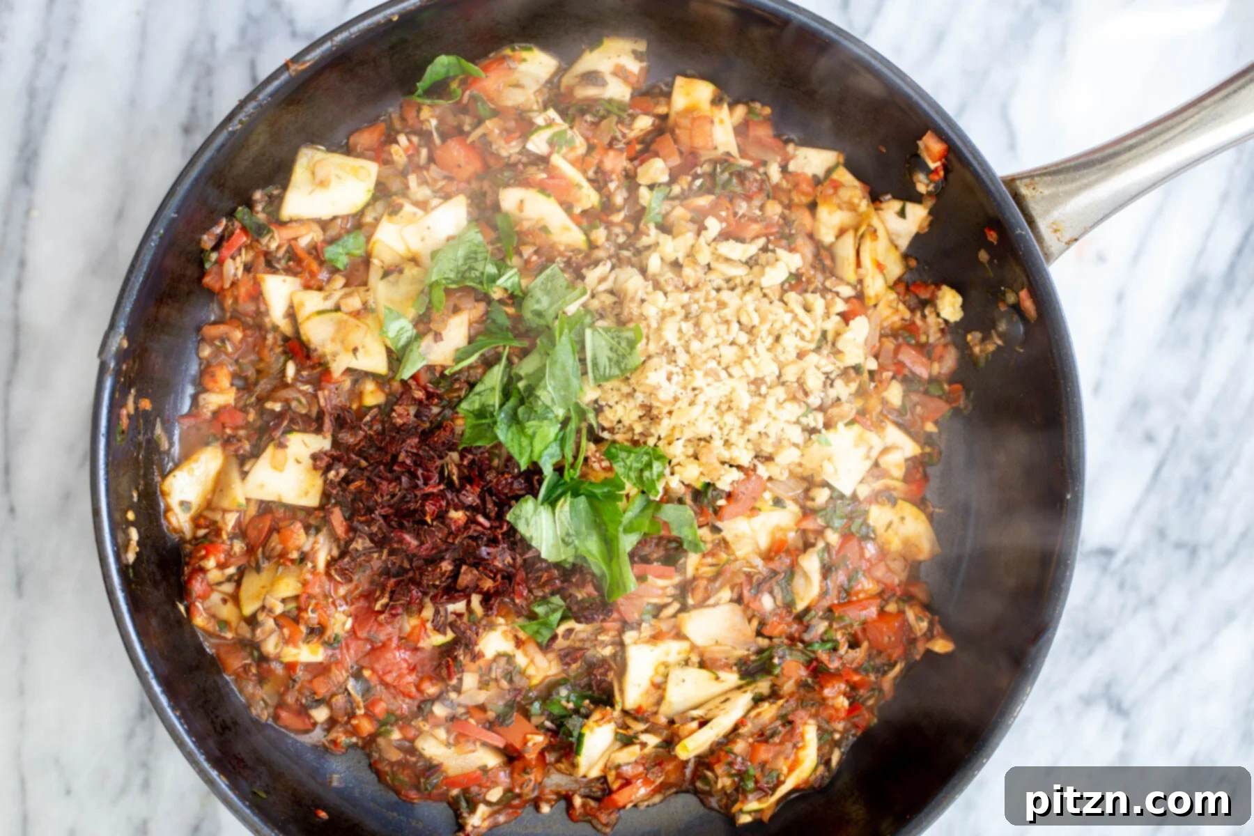 Fresh basil and sun-dried tomatoes mingling with the cooked vegetables in a sautéing pan, adding freshness and depth to the pasta.