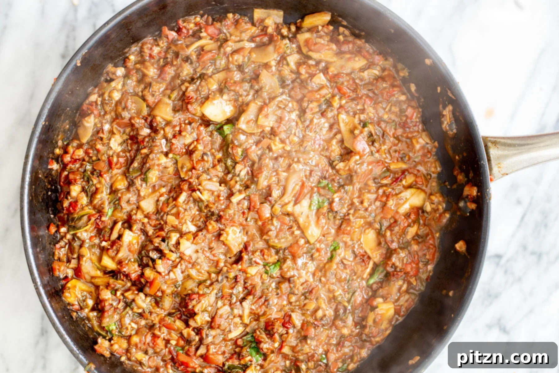 Vegetable ragu with chopped walnuts in a black sautéing pan, a hearty and flavorful base for the pasta.