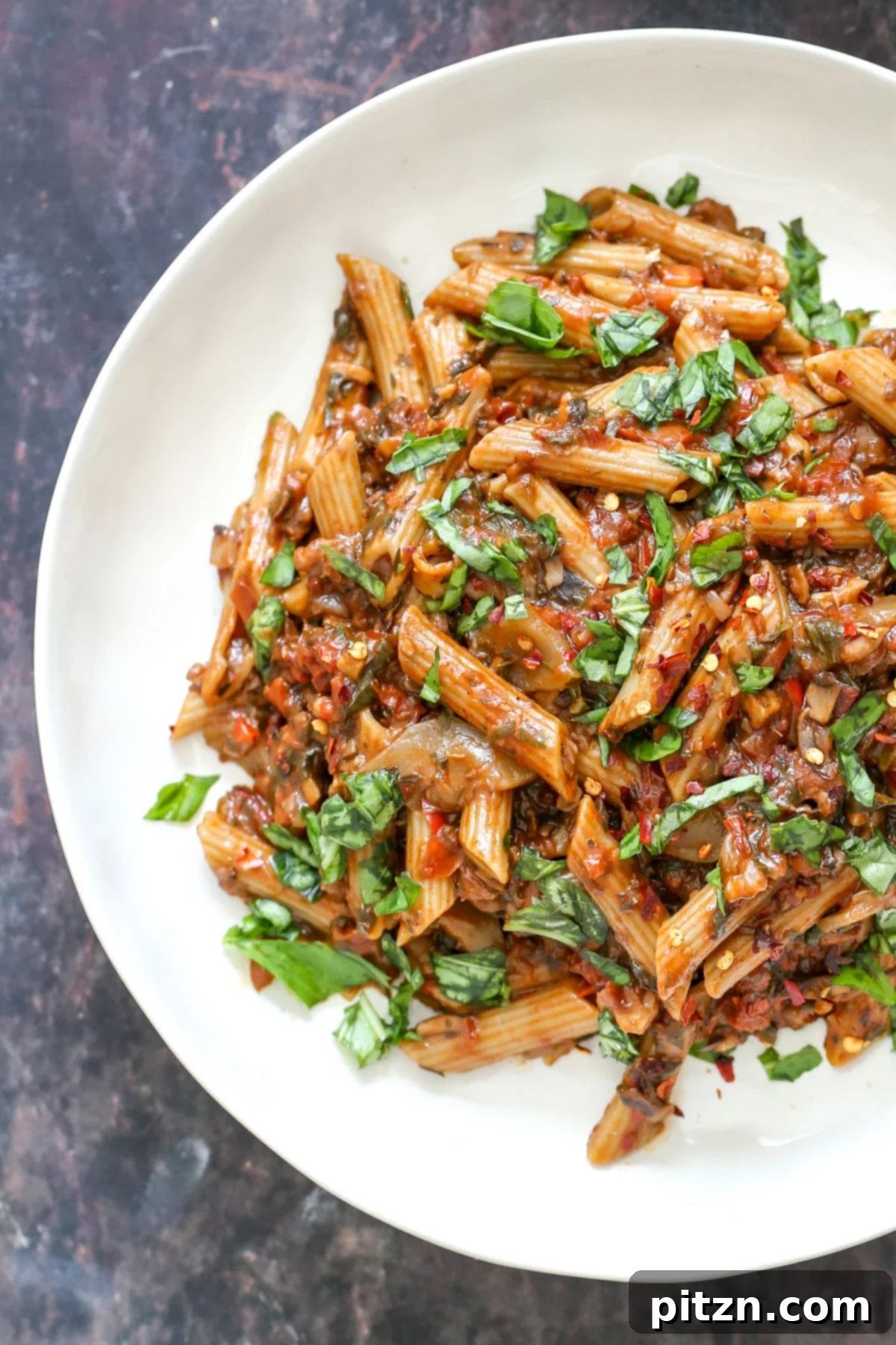 Serving of Penne pasta with walnut, sun-dried tomato sauce, and fresh basil on a white plate.