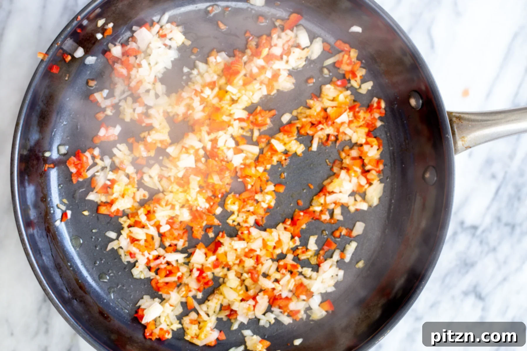 Red chili flakes, garlic, and onion sautéing in a black pan, fragrant and ready for the next step of the pasta.