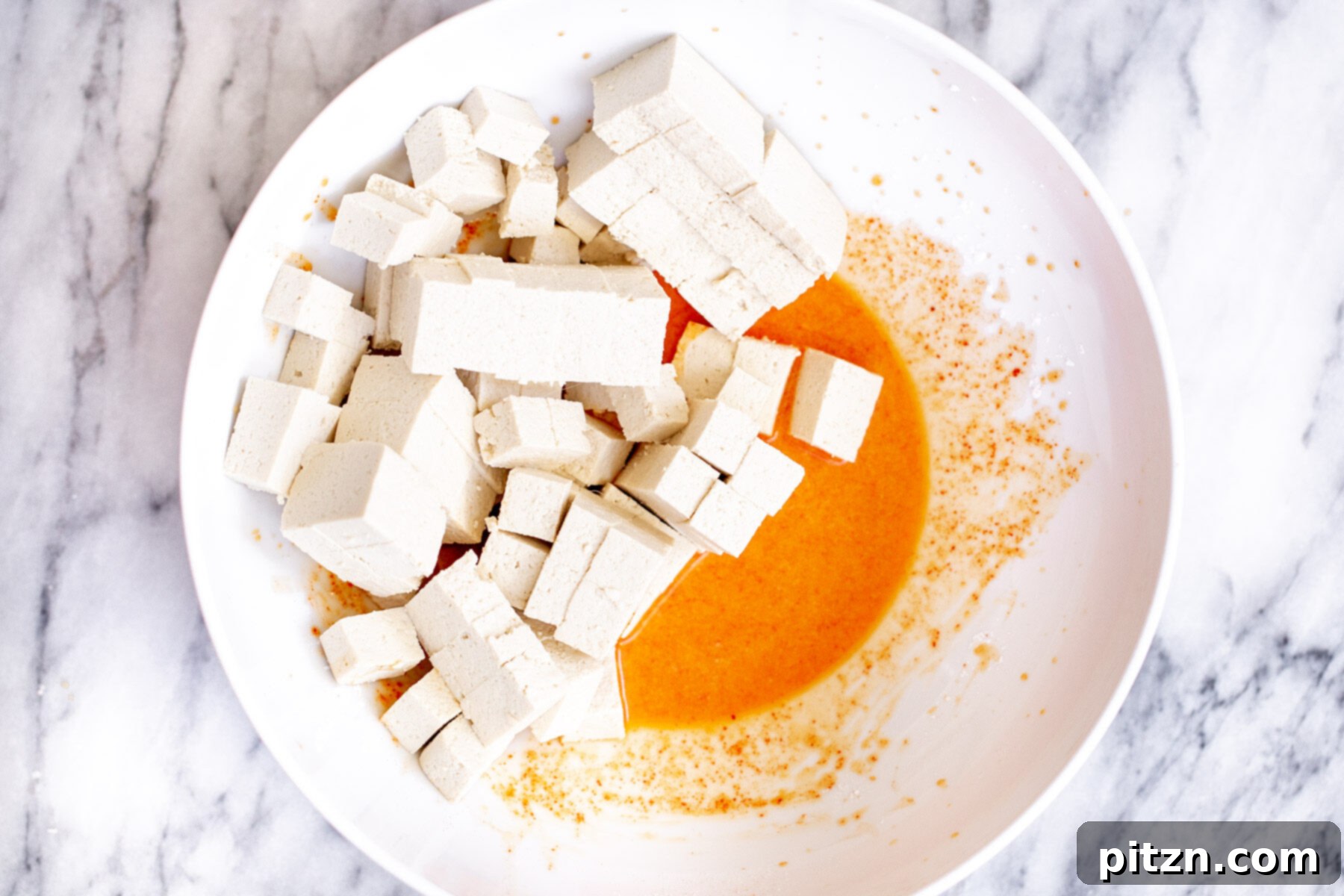 Cubed tofu pieces thoroughly mixed with spices and cornstarch in a white bowl, ready for cooking.