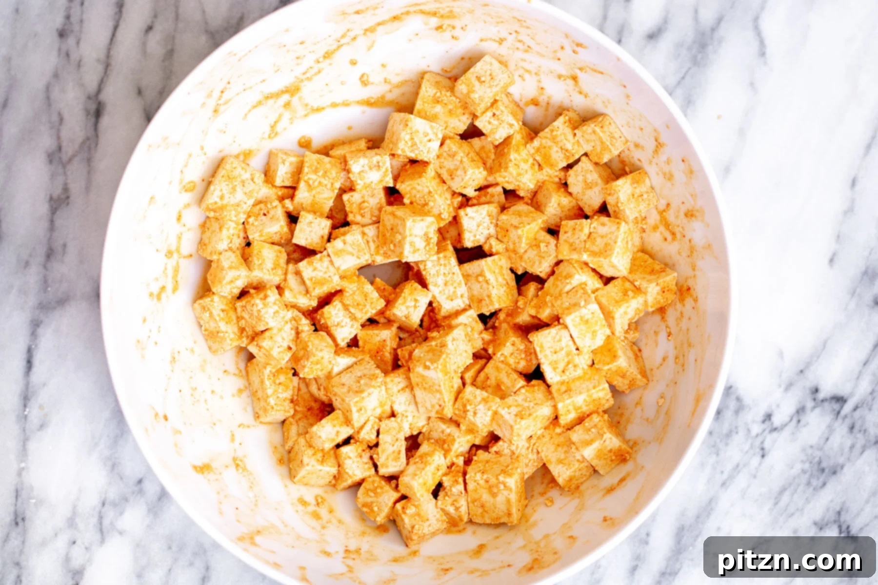 Another view of the spiced tofu cubes in a white bowl, showcasing the even coating of the marinade.