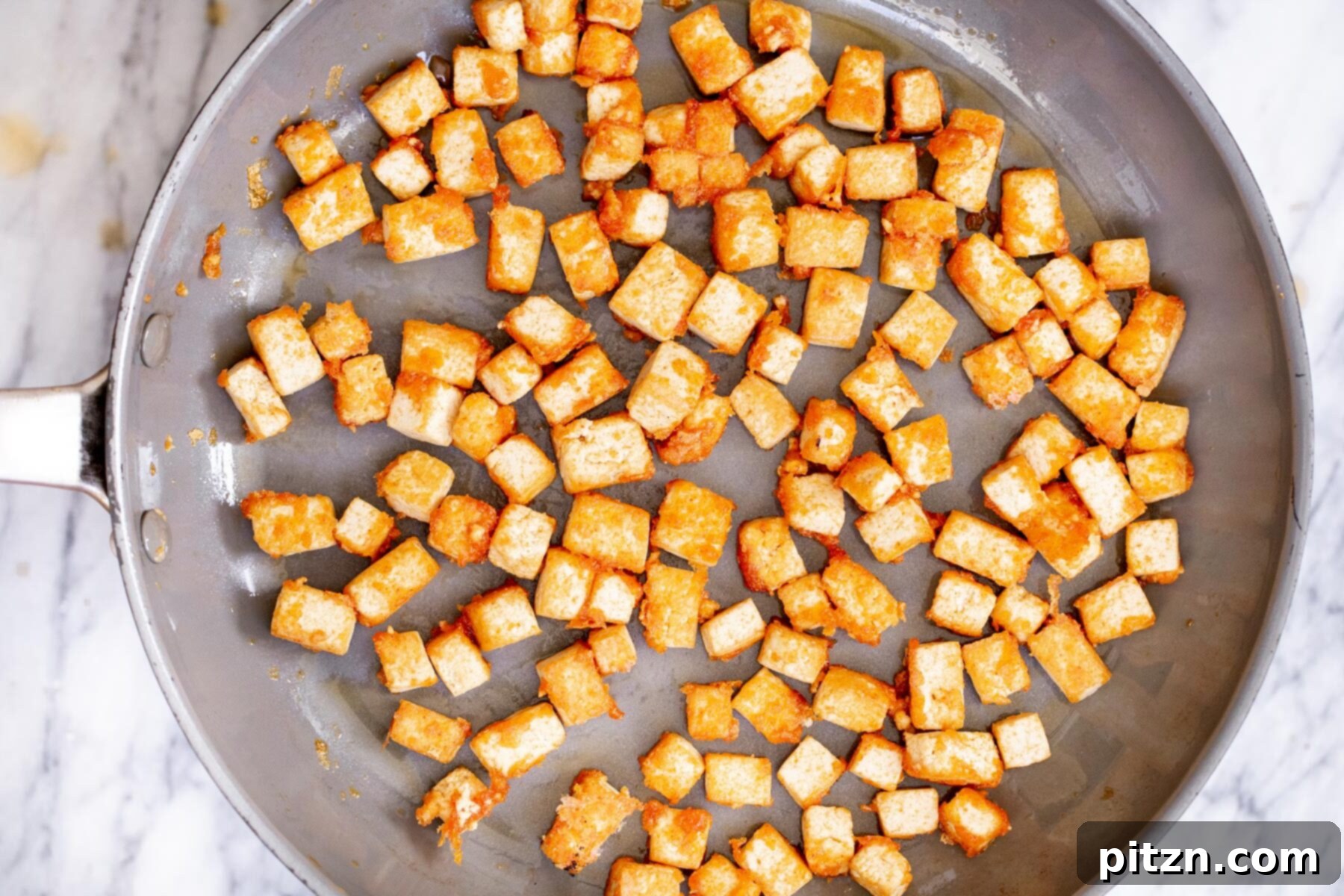 Crispy, golden-brown tofu cubes sizzling in a black sauteing pan after being pan-seared to perfection.