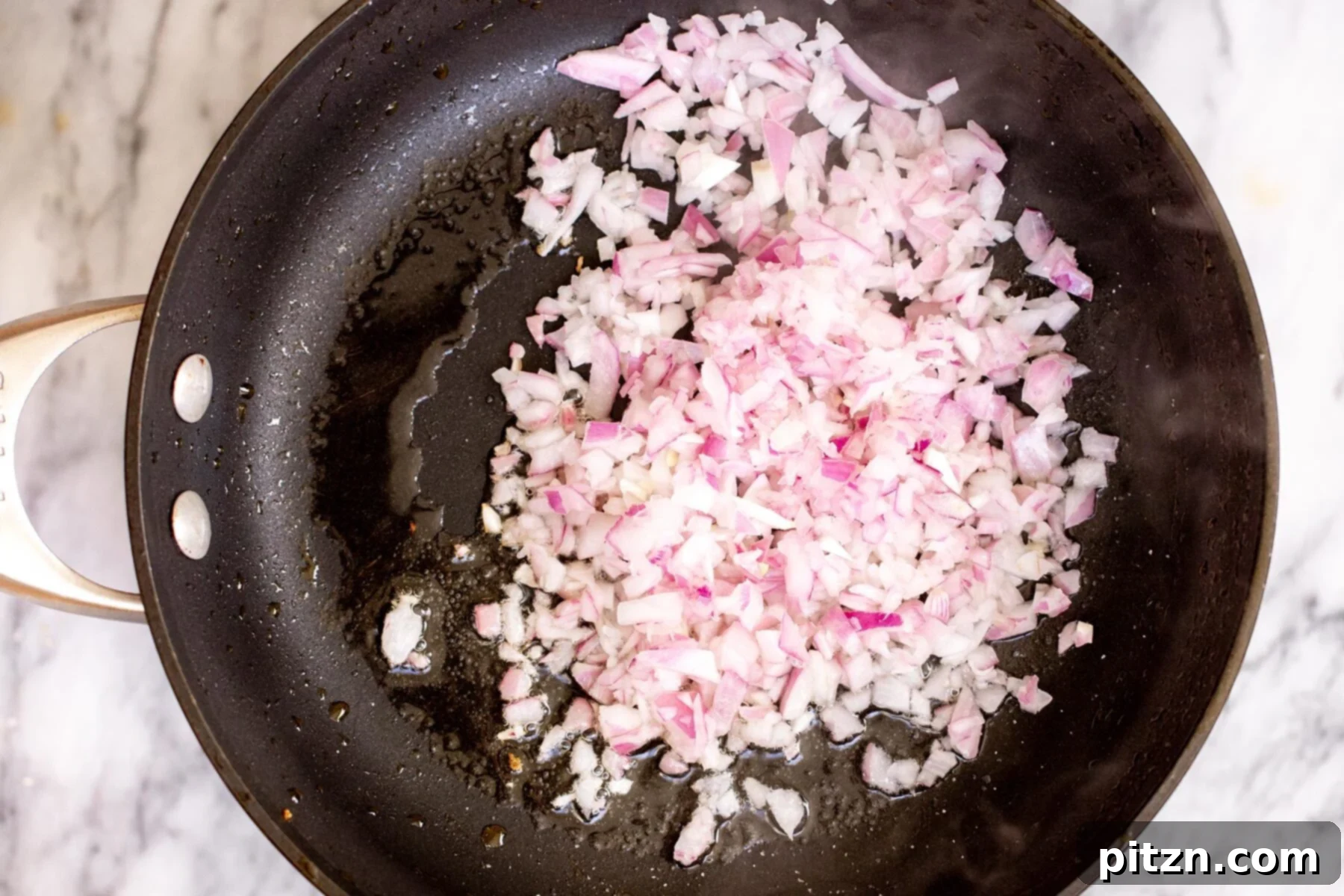 Finely chopped red onions sautéing in a black non-stick pan, beginning to soften and caramelize.