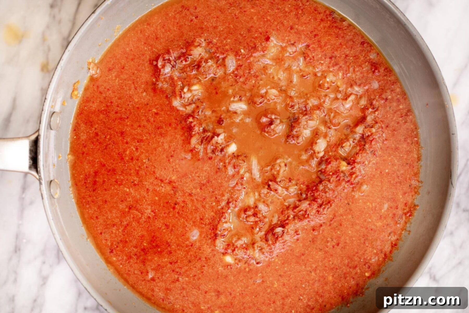 The rich, red spice paste being carefully added to the pan with the sautéed golden onions, beginning to form the vindaloo gravy.